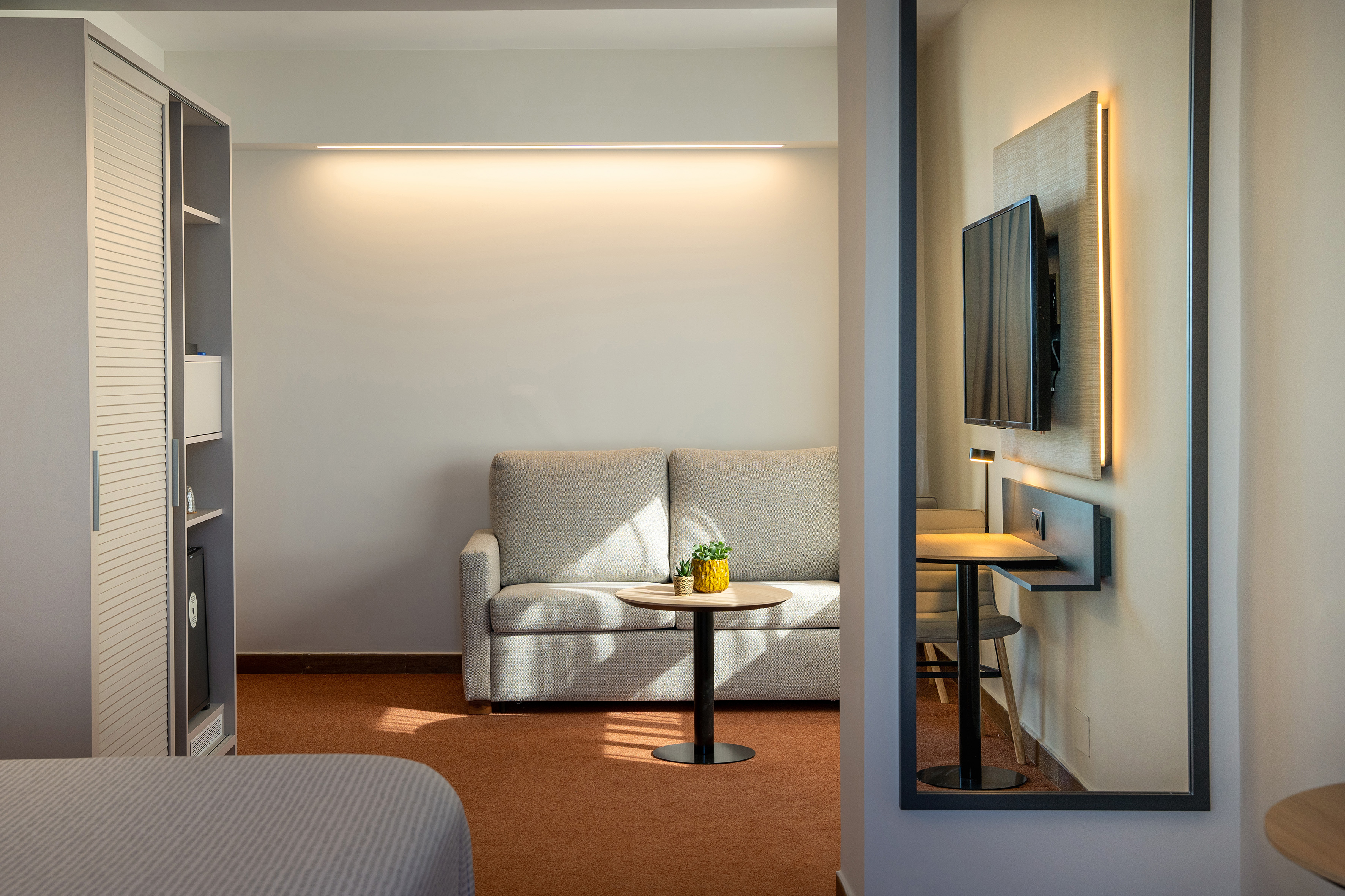 Modern hotel suite living area with sofa, wall TV, and desk.