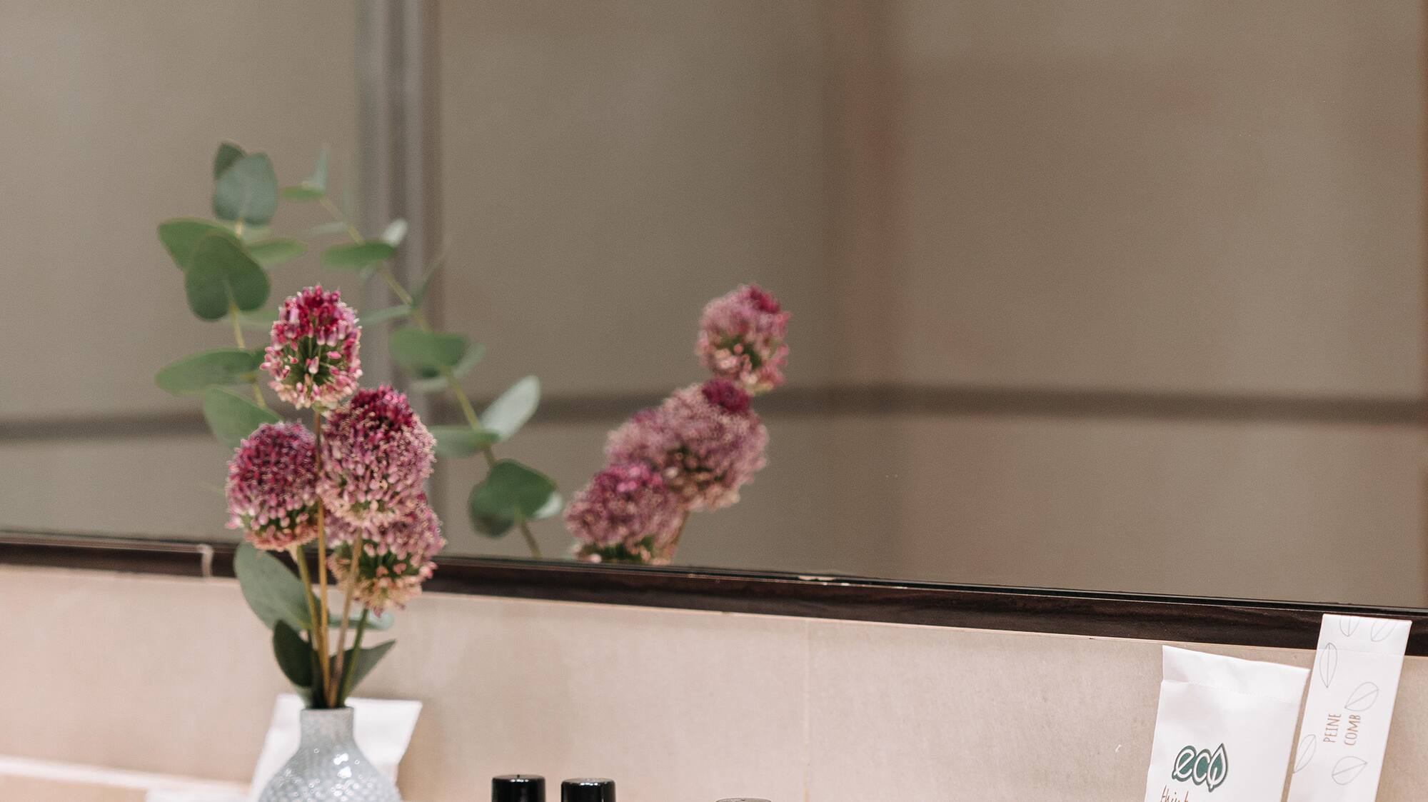 a bathroom mirror with a vase of flowers and other objects