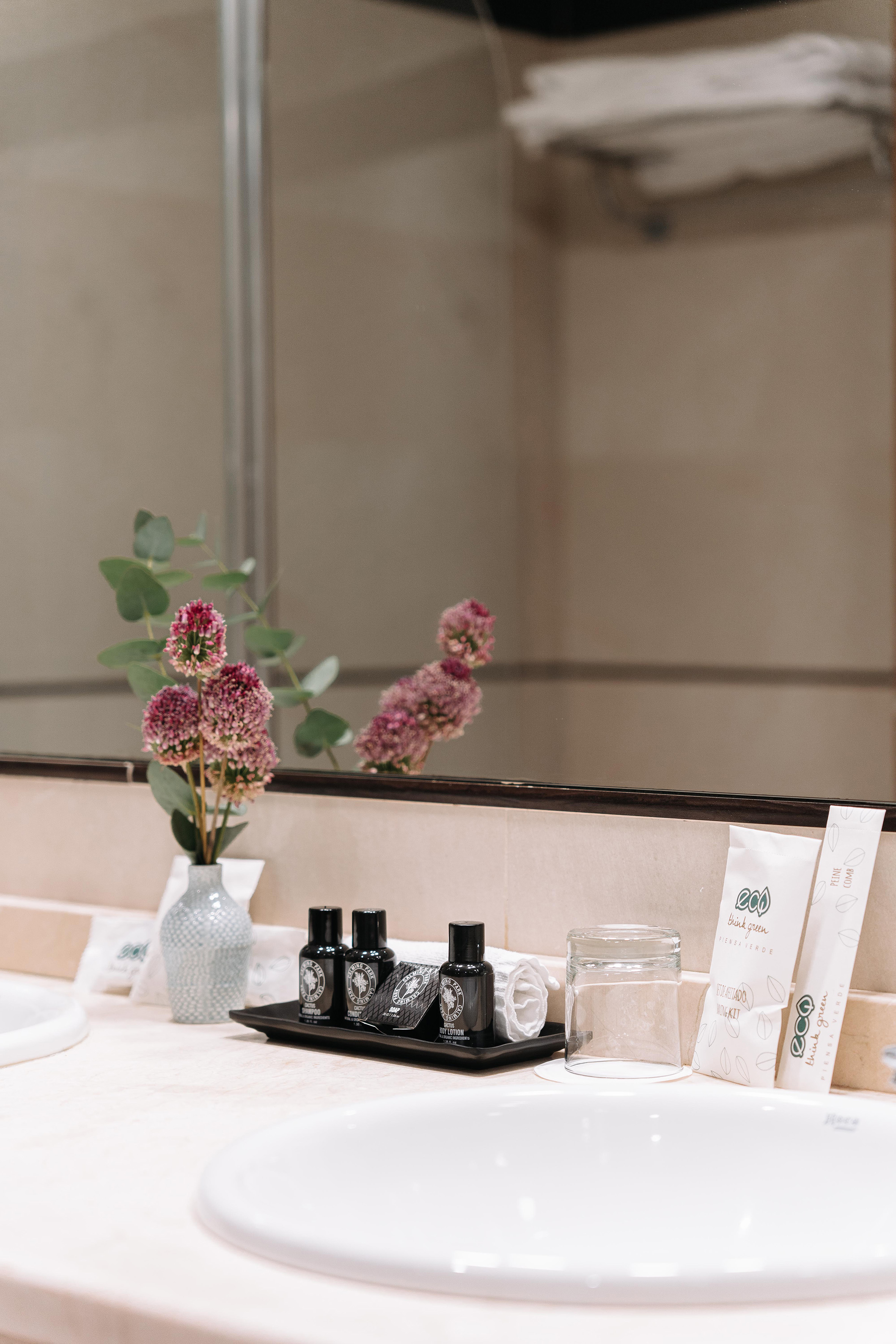 Hotel bathroom vanity with eco-friendly toiletries, pink flowers, and mirror.