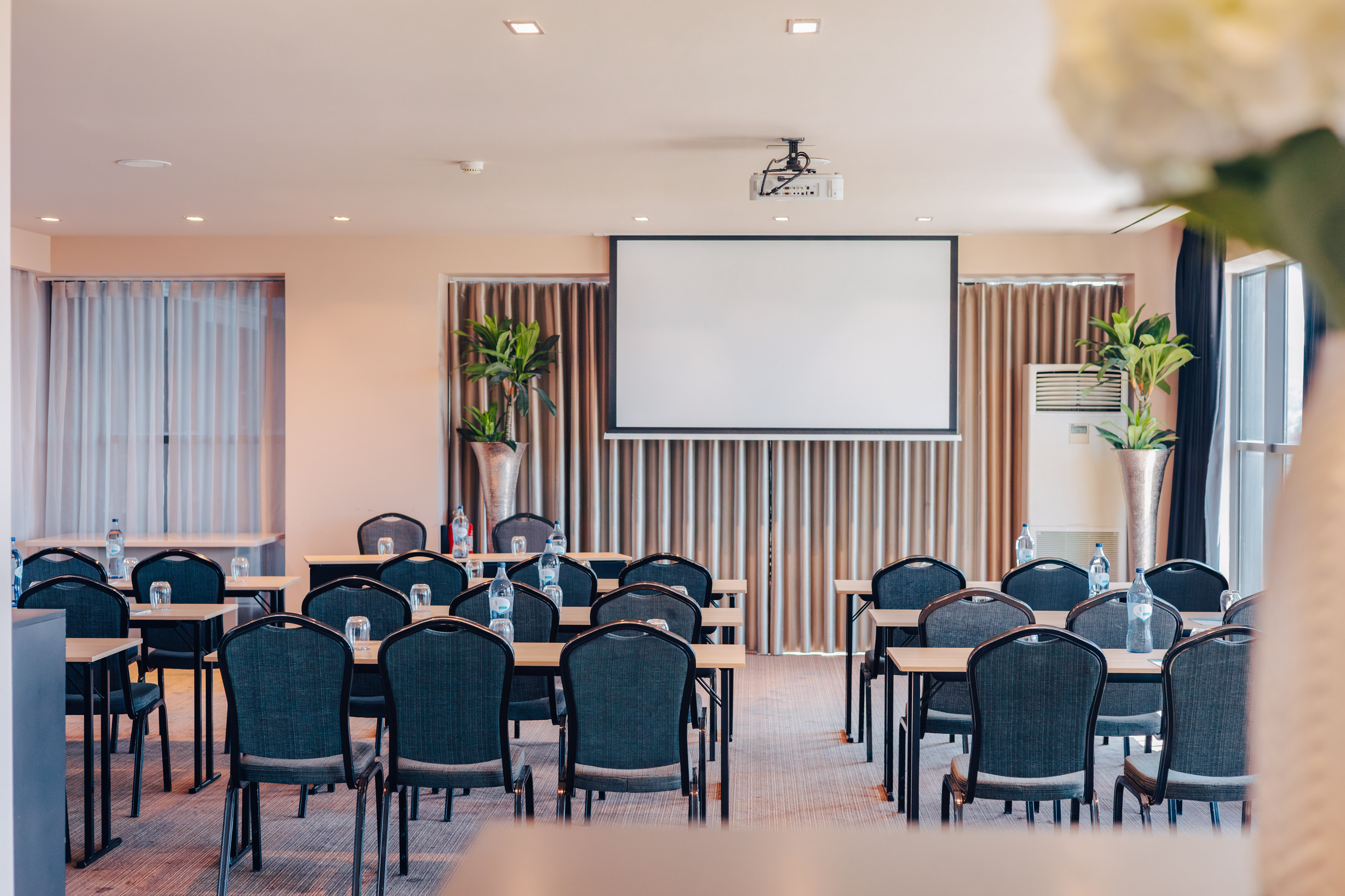 Conference room setup with projector screen, tables, chairs, and bottled water.