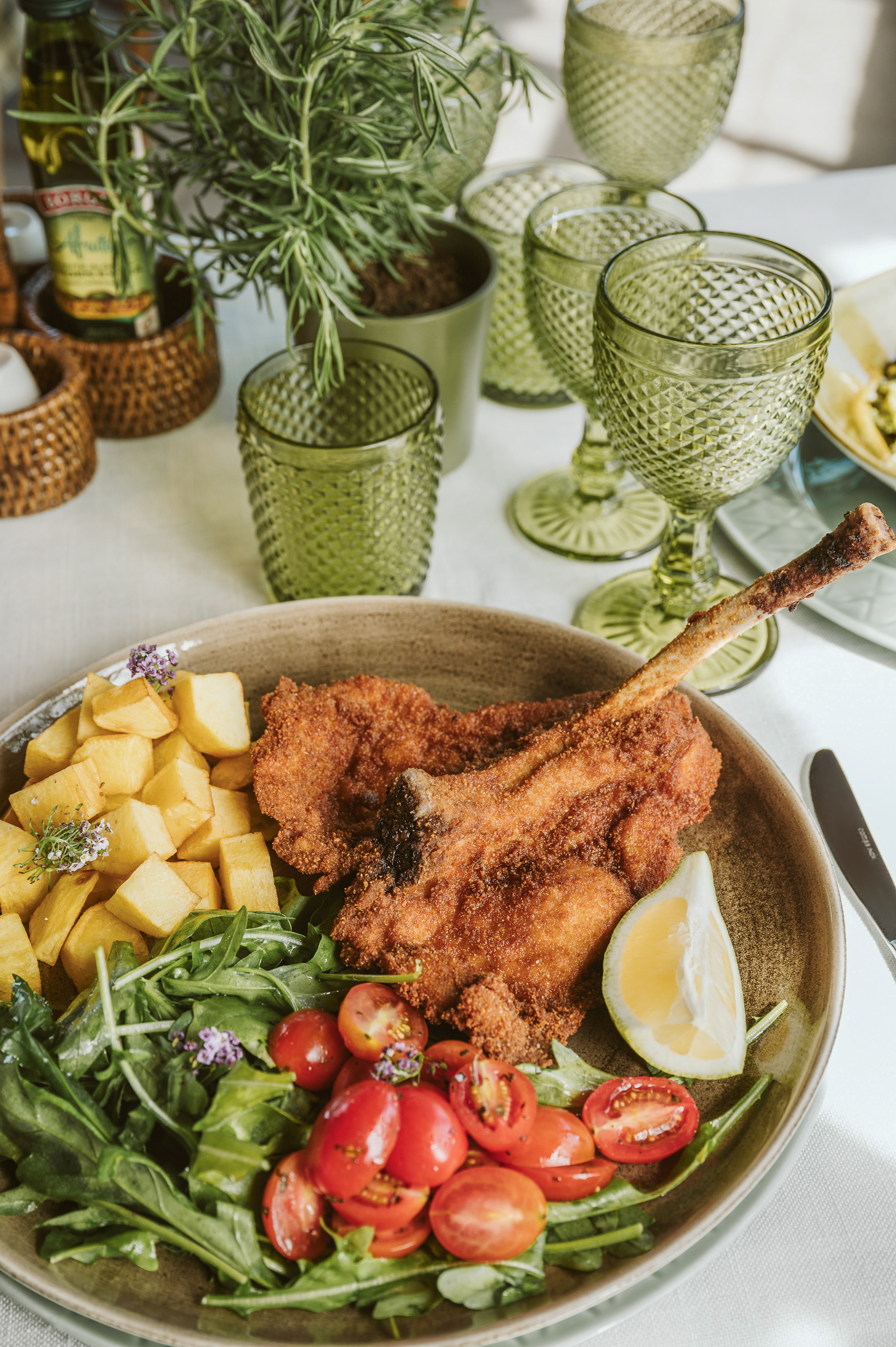 Crispy breaded cutlet, fried potatoes, green salad, tomatoes, lemon wedge.