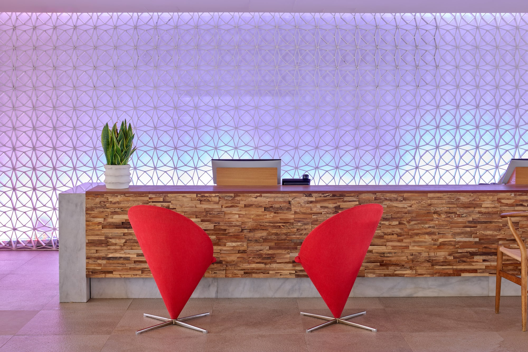 Hotel reception with wood counter, two red chairs, and geometric backlit wall.