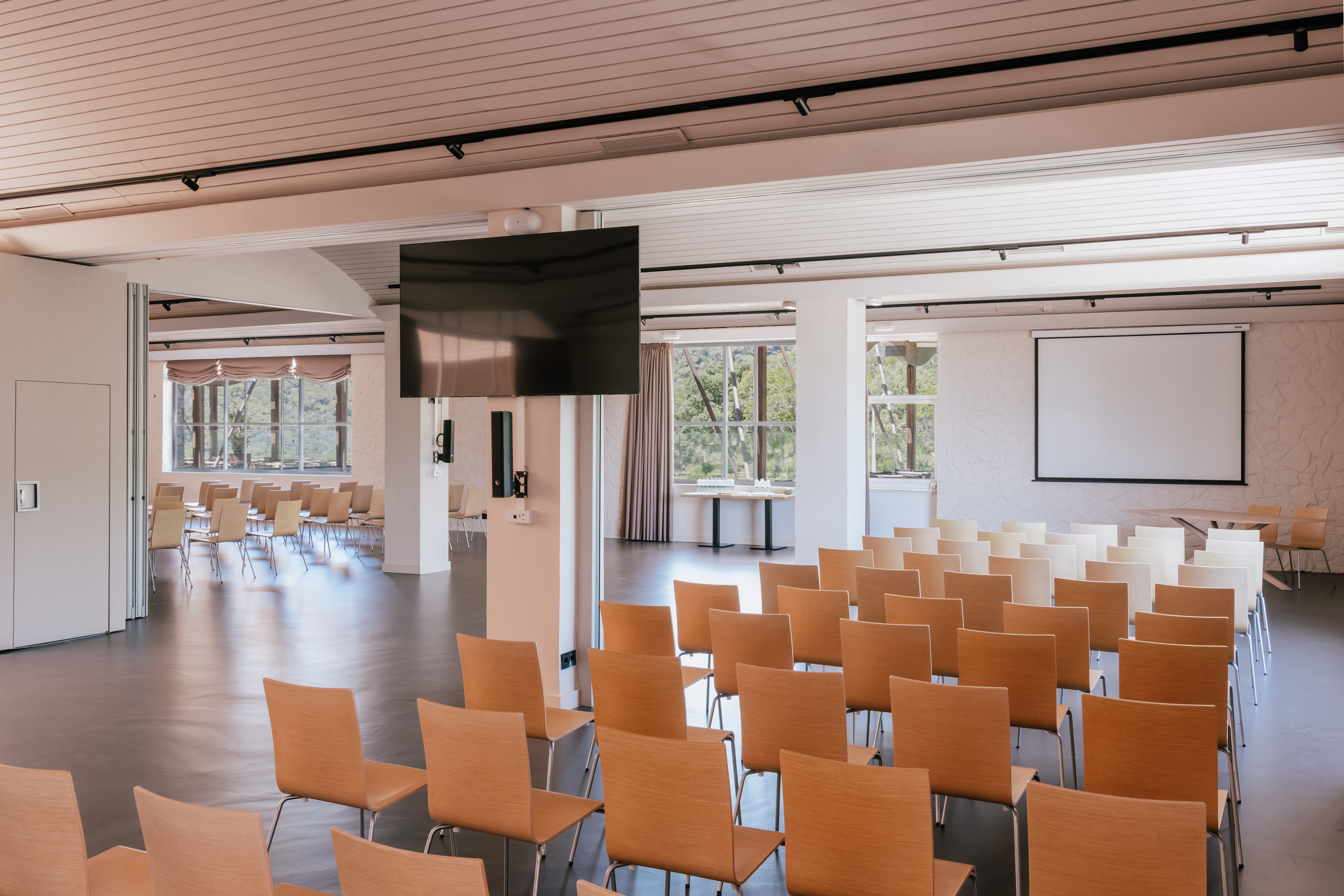 Empty modern event room with wooden chairs, large TV, and projector screen.