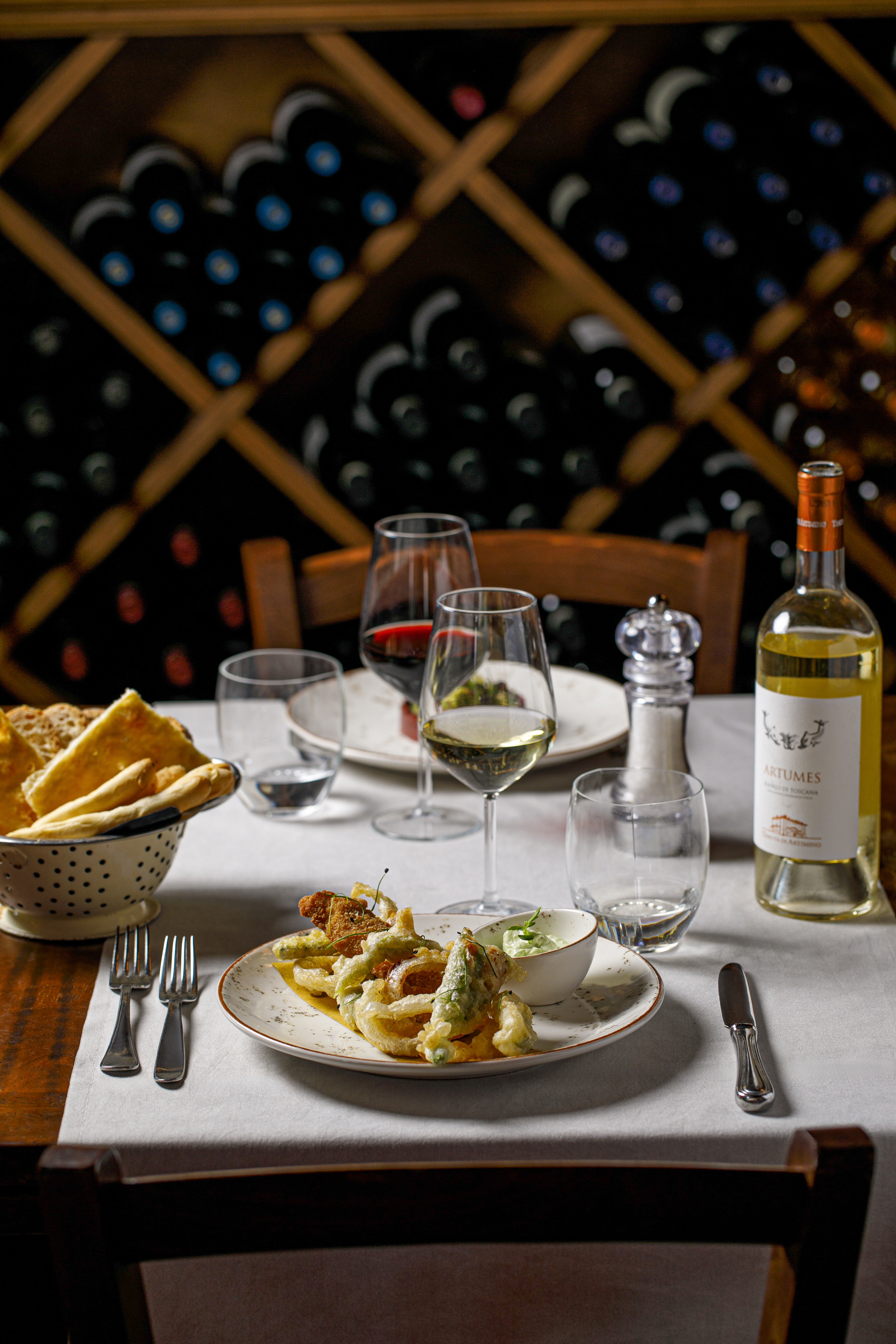Fried appetizer, white and red wine on a dining table in front of a wine rack.