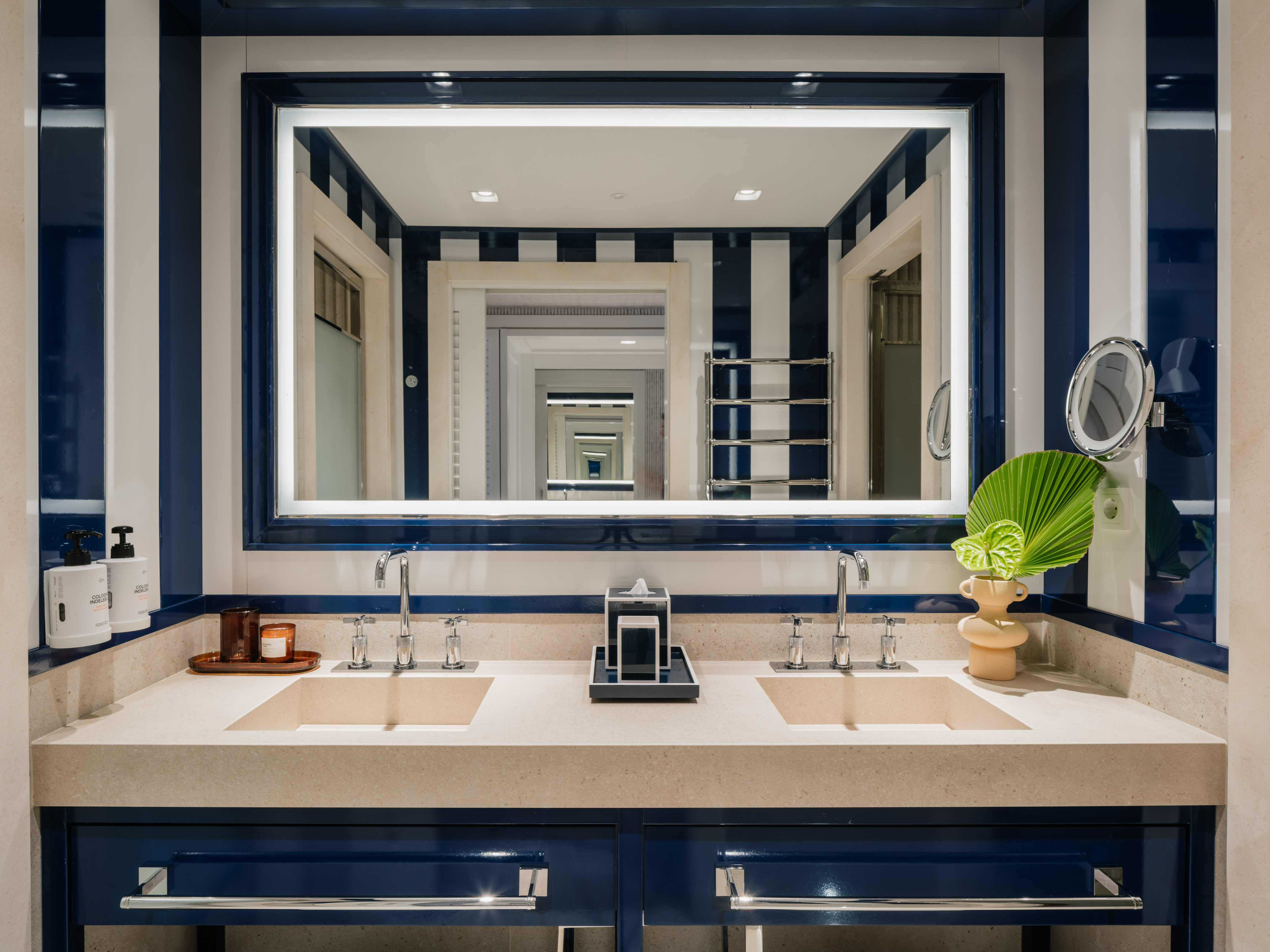 Bathroom with blue and white striped walls, double vanity, and lit mirror.