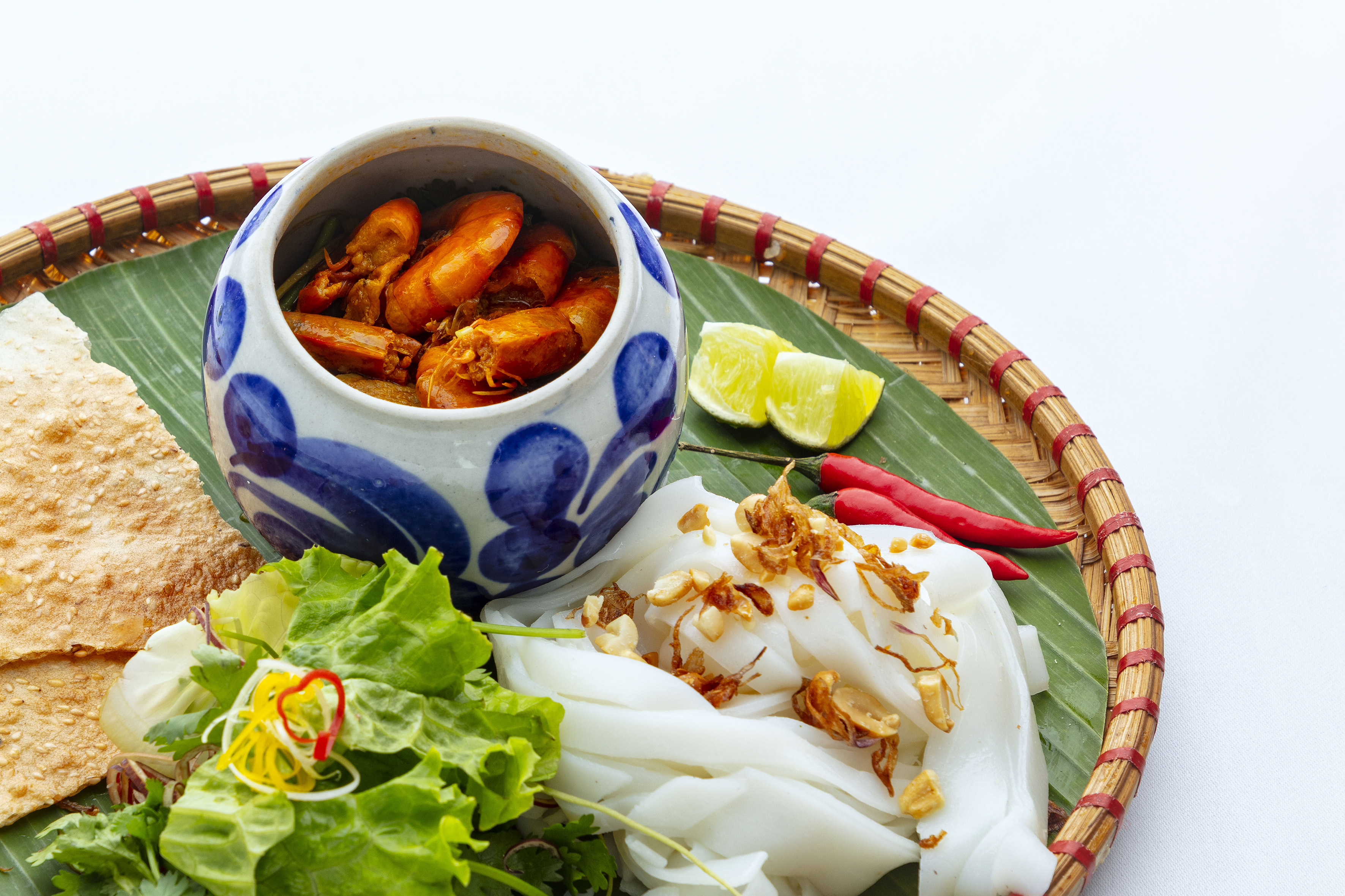 Vietnamese shrimp, rice noodles, fresh greens, and cracker on a woven tray.