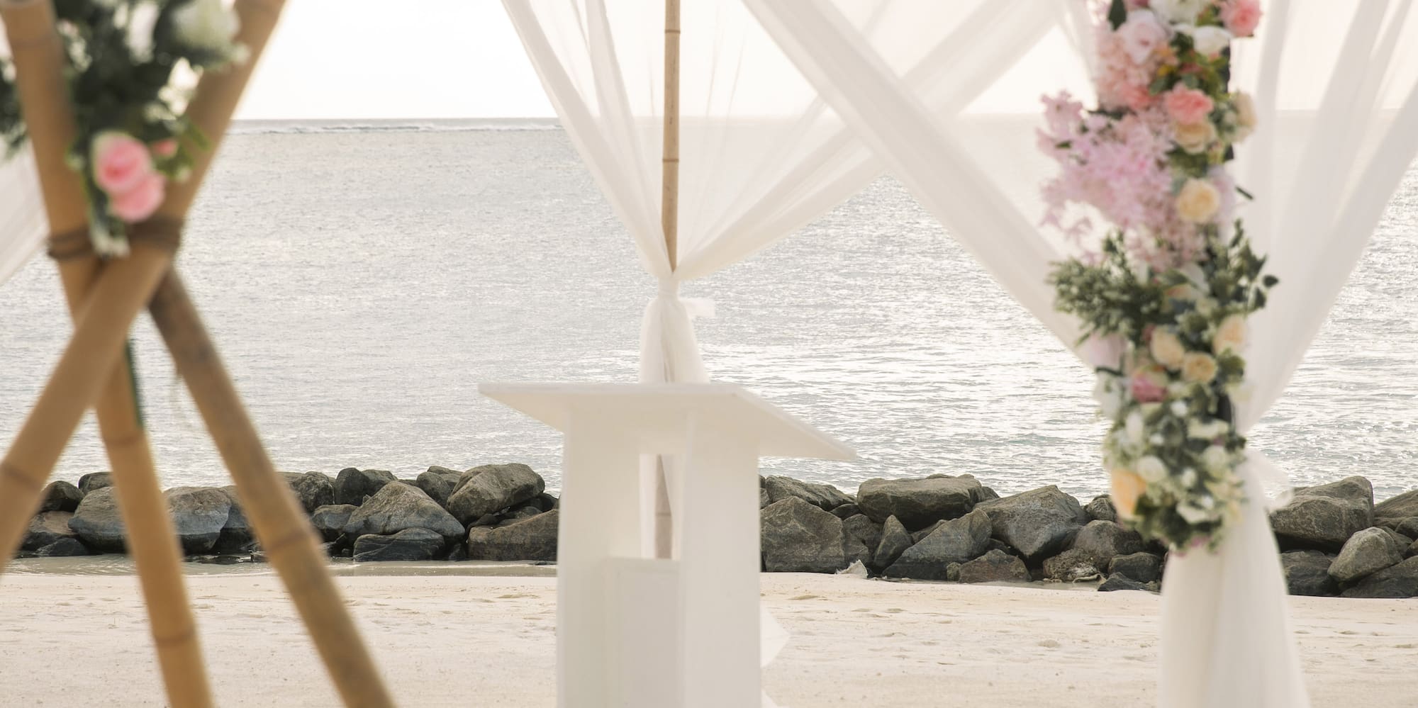 a white tent with flowers and a white curtain on the beach