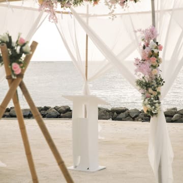 a white tent with flowers and a white curtain on the beach