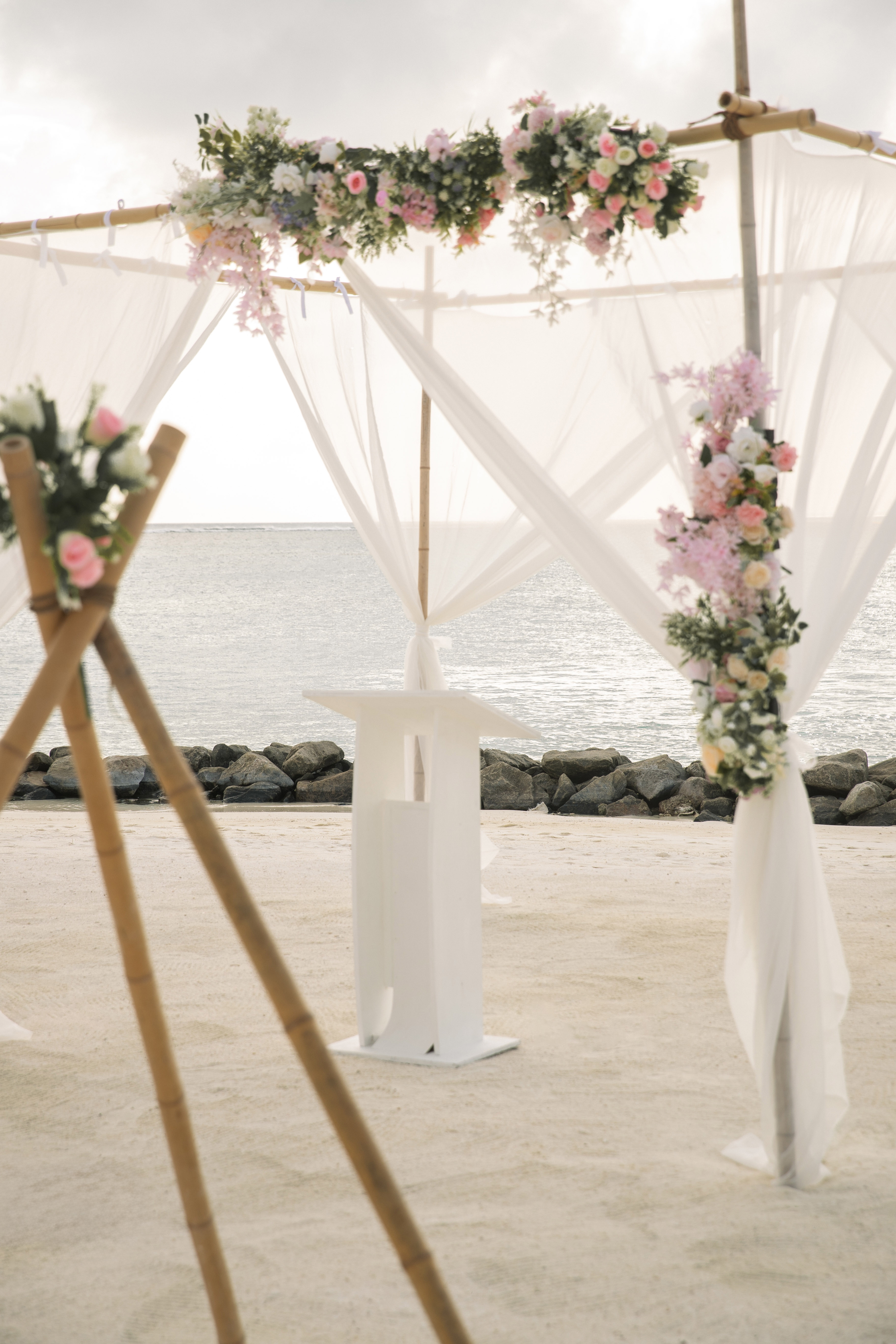 Bamboo beach wedding arch with pink and white flowers, ocean view.