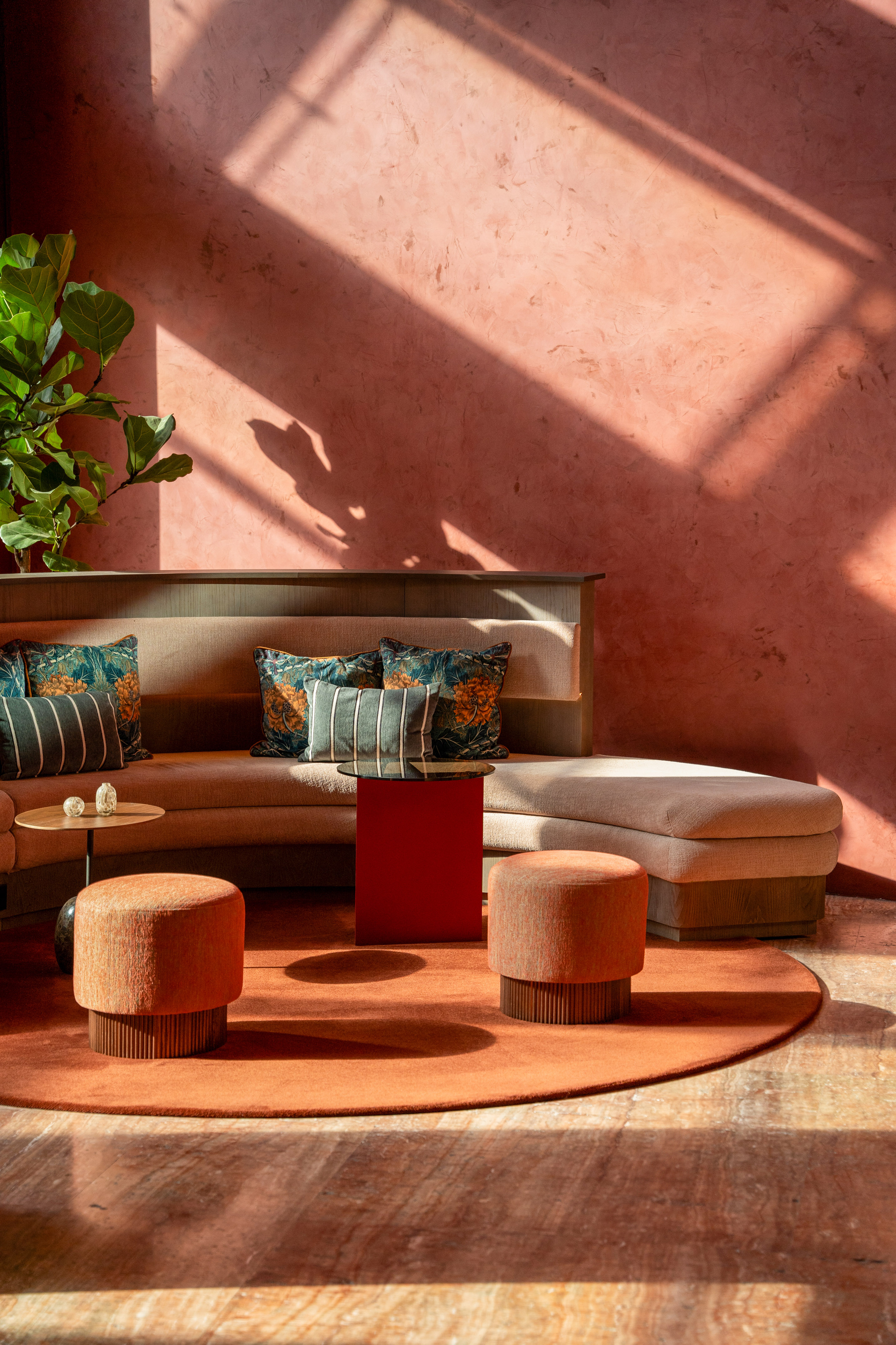 Contemporary lounge with terracotta wall, beige sofa, orange ottomans, sunlight.