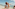 Smiling man lifts happy child high on a sunny beach by the ocean.