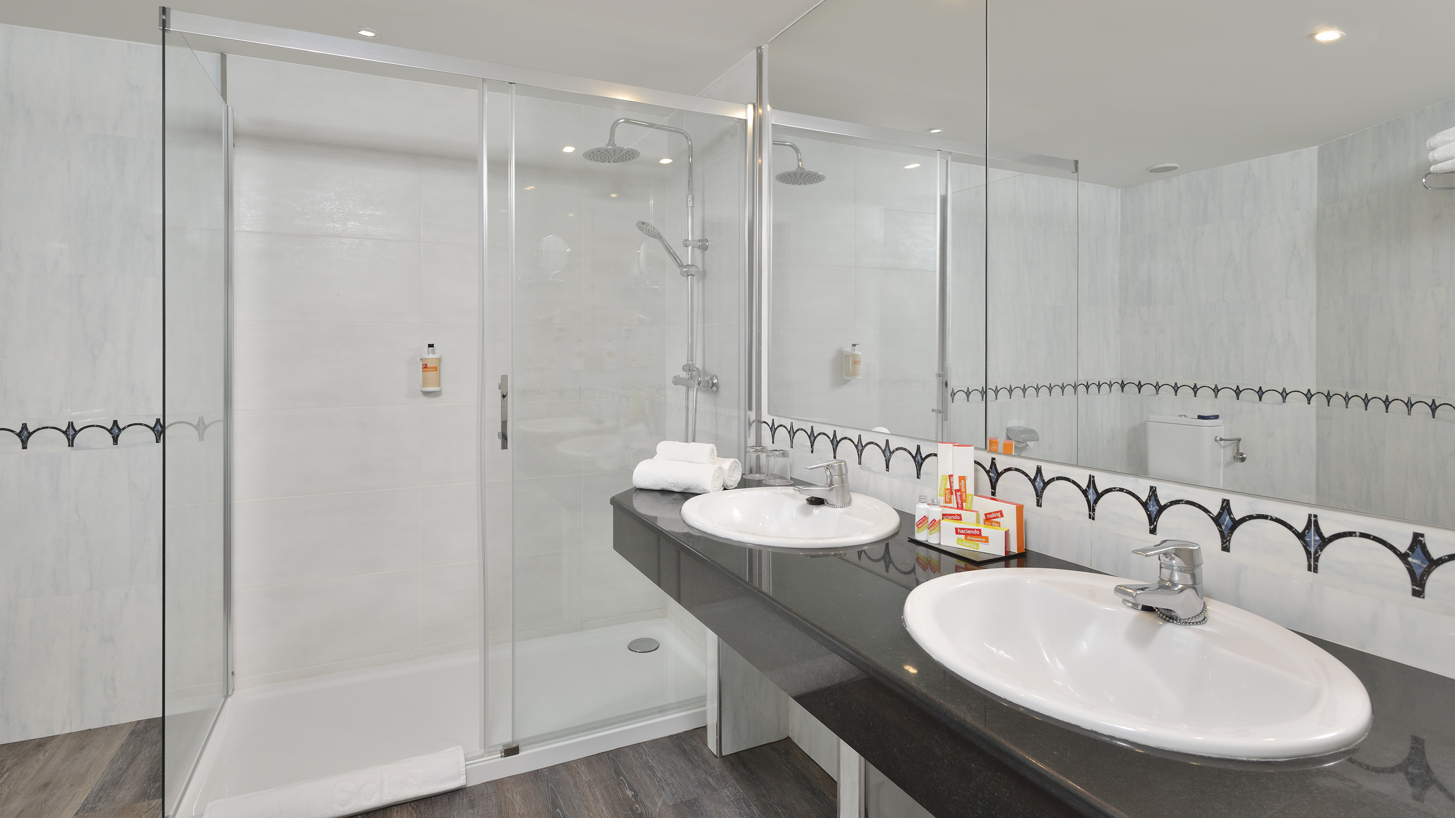 Modern hotel bathroom with dual sinks, dark vanity, and glass enclosed shower.