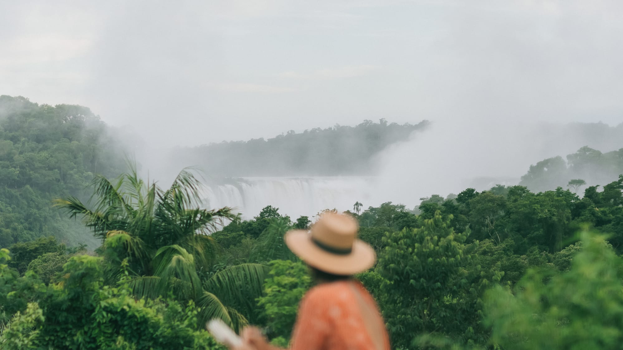 a woman sitting on a ledge looking at a waterfall