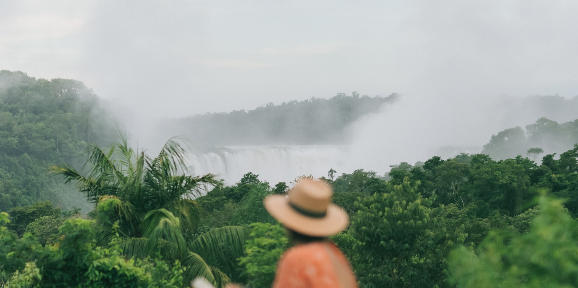 a woman sitting on a ledge looking at a waterfall