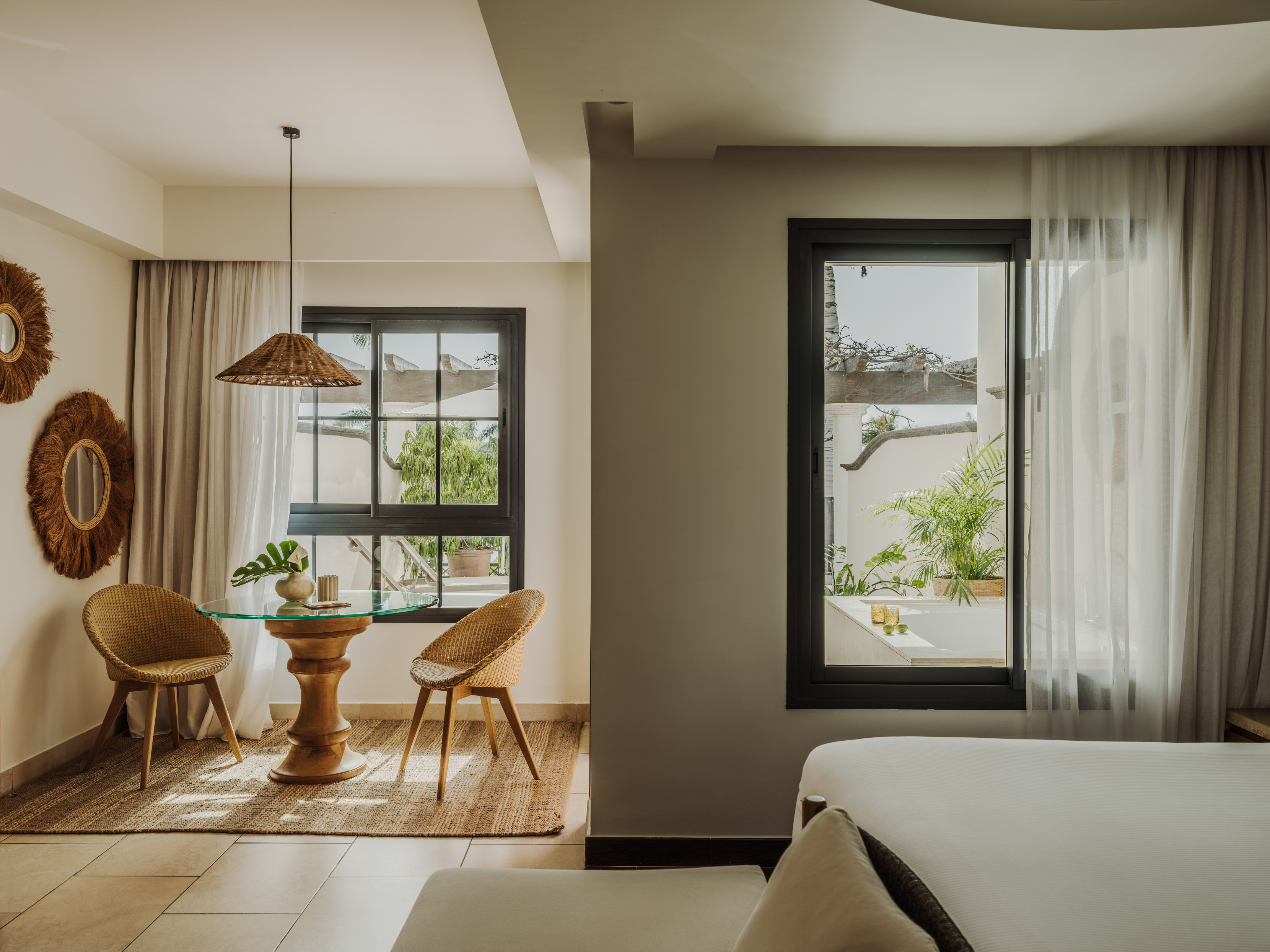 Tropical resort suite with wicker dining, bedroom, and private garden patio.