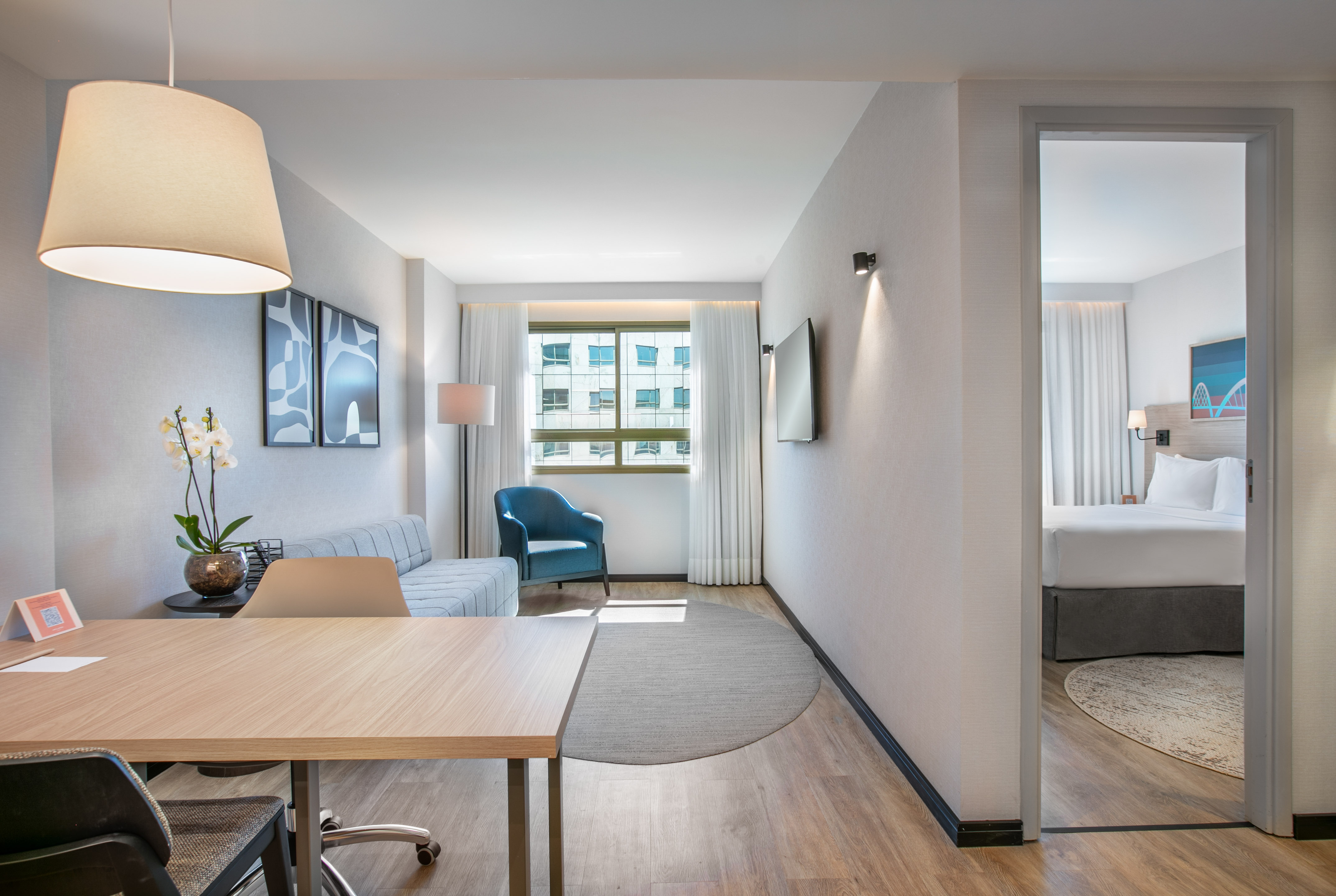 Modern hotel suite with living area, work desk, sofa, and adjacent bedroom.