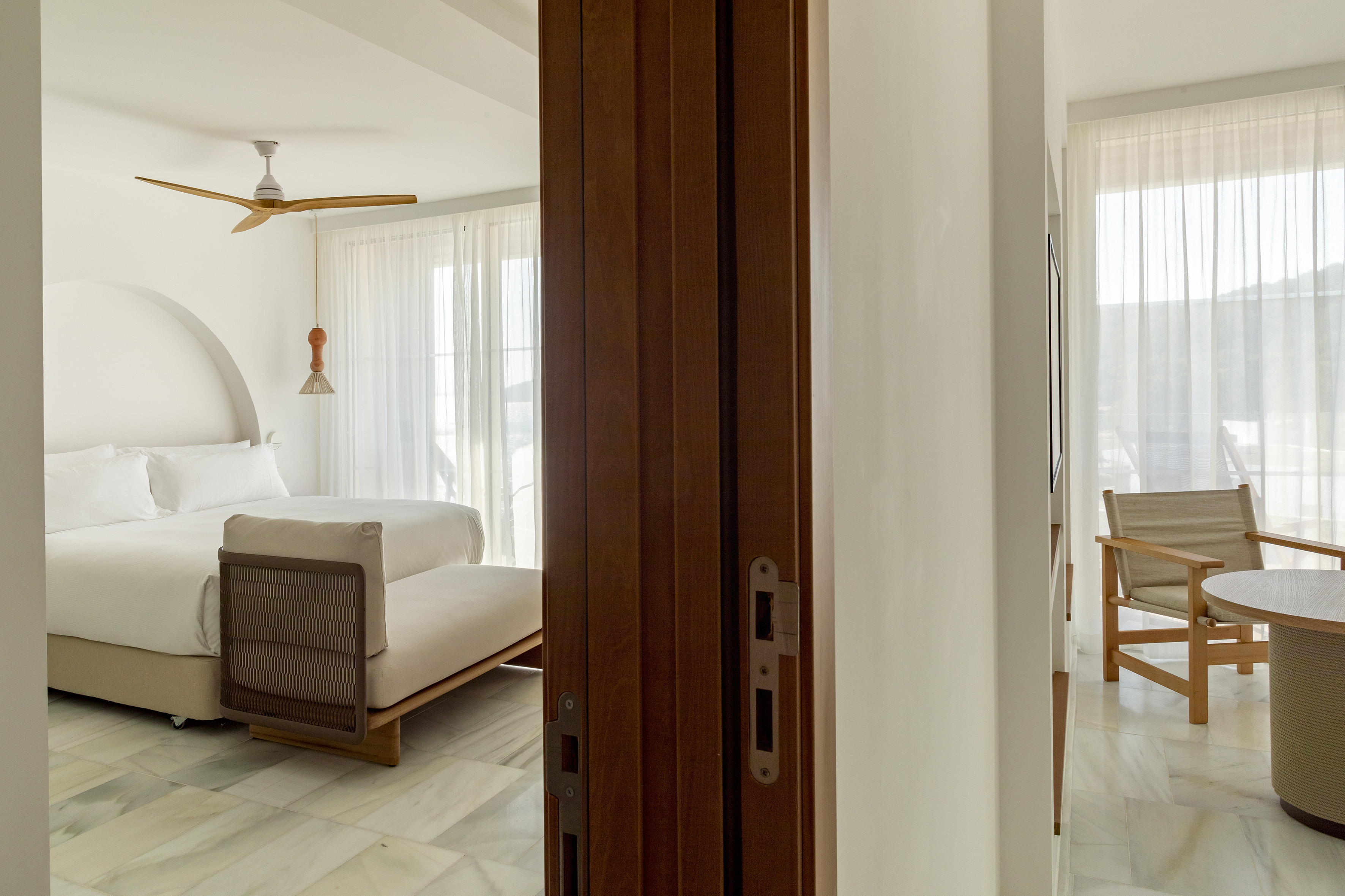 Modern bedroom with white bed, marble floor, wooden ceiling fan, open folding door.