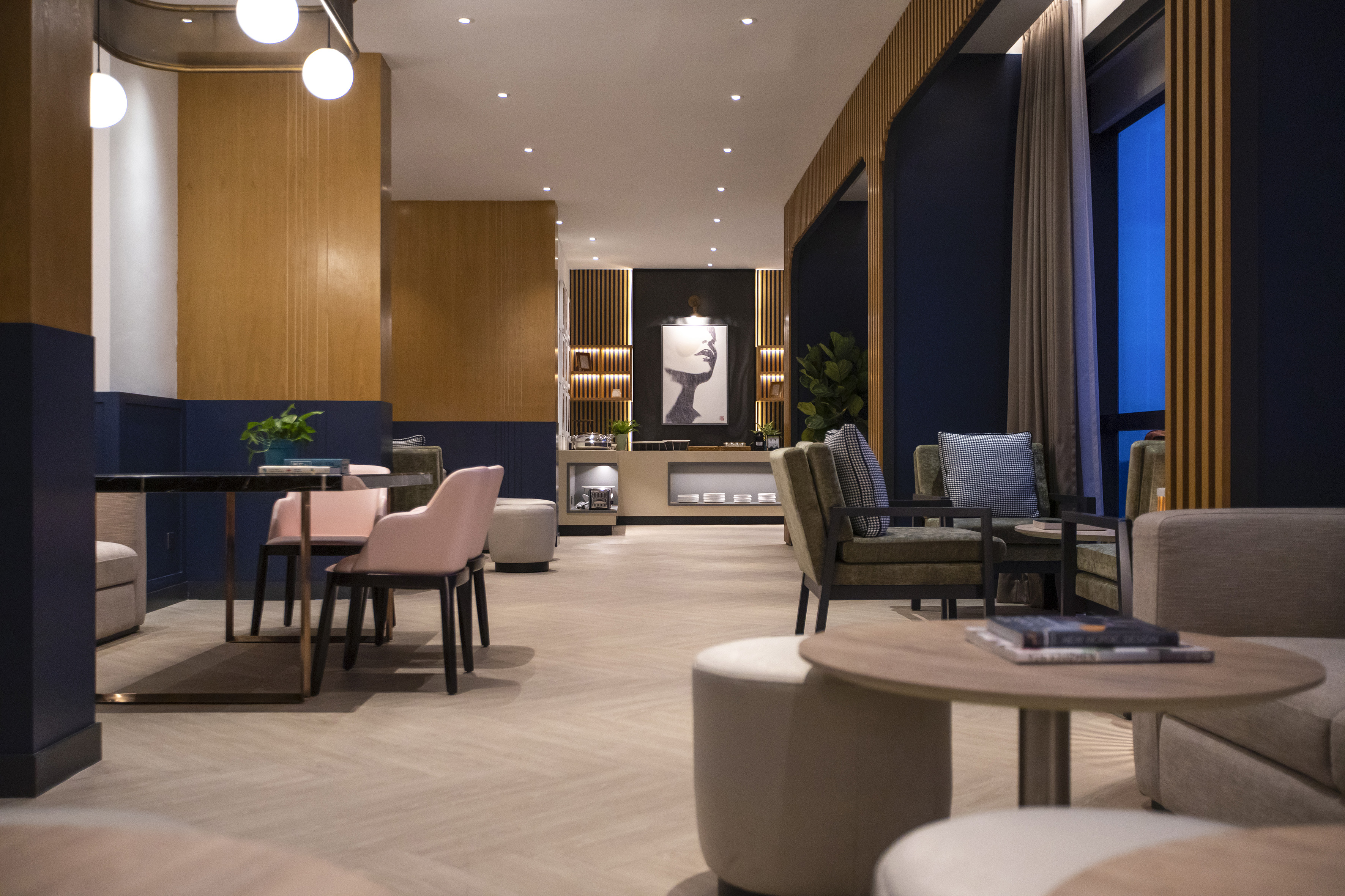 Modern lounge interior with wood panels, blue walls, diverse seating, and warm lighting.