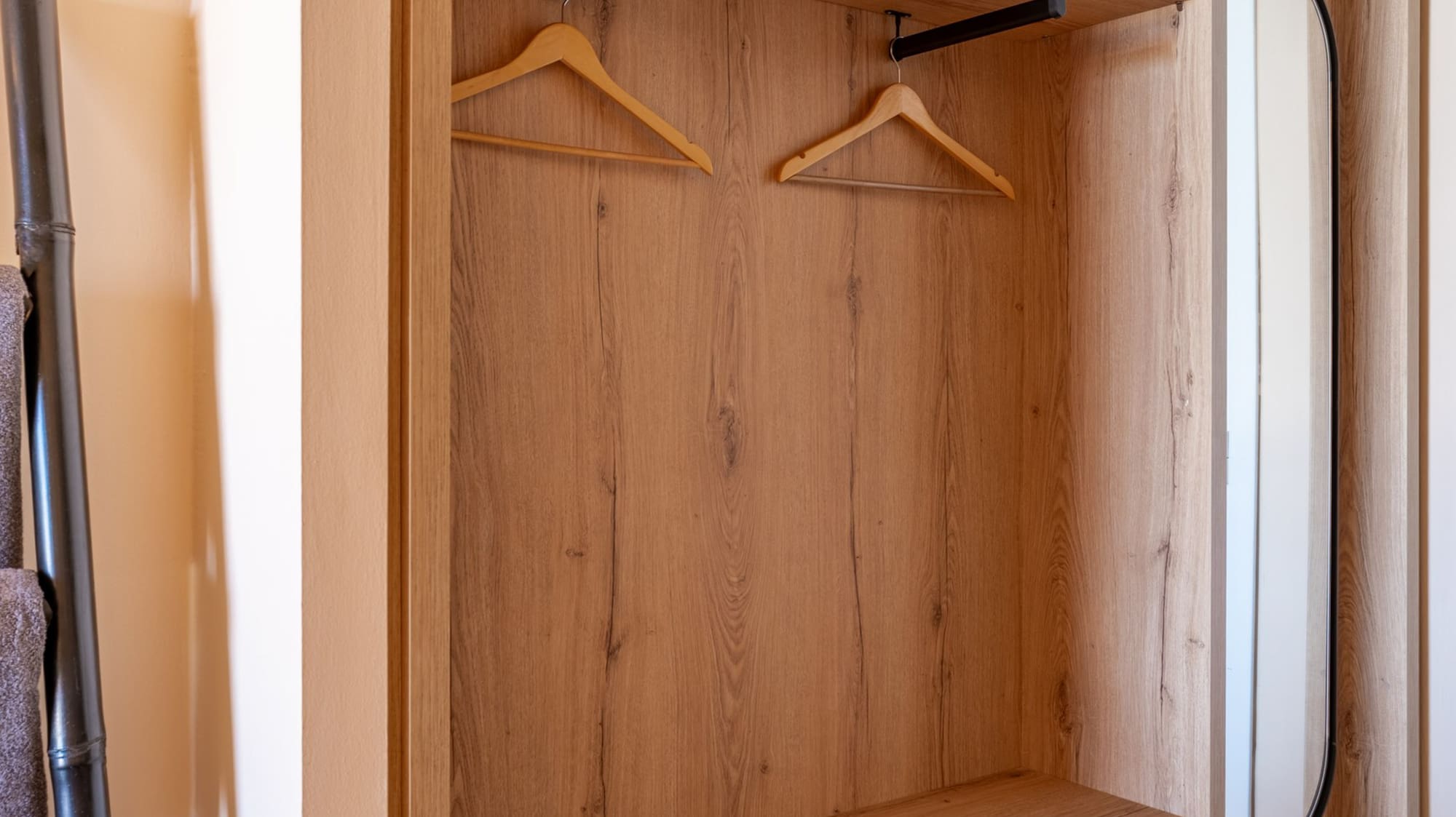 Modern light wood open wardrobe with hangers, shelves, and integrated mirror.