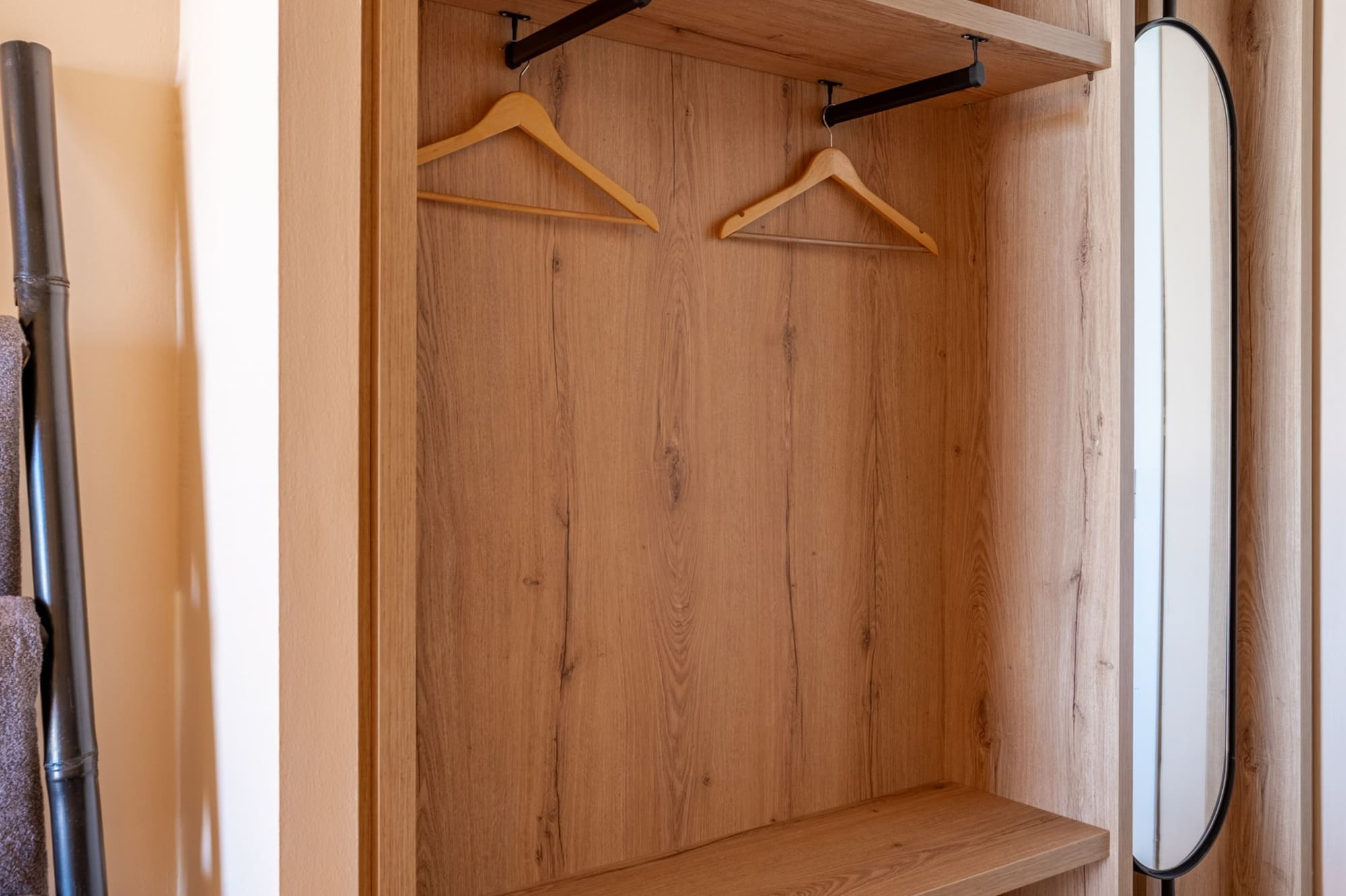 Modern light wood open wardrobe with hangers, shelves, and integrated mirror.