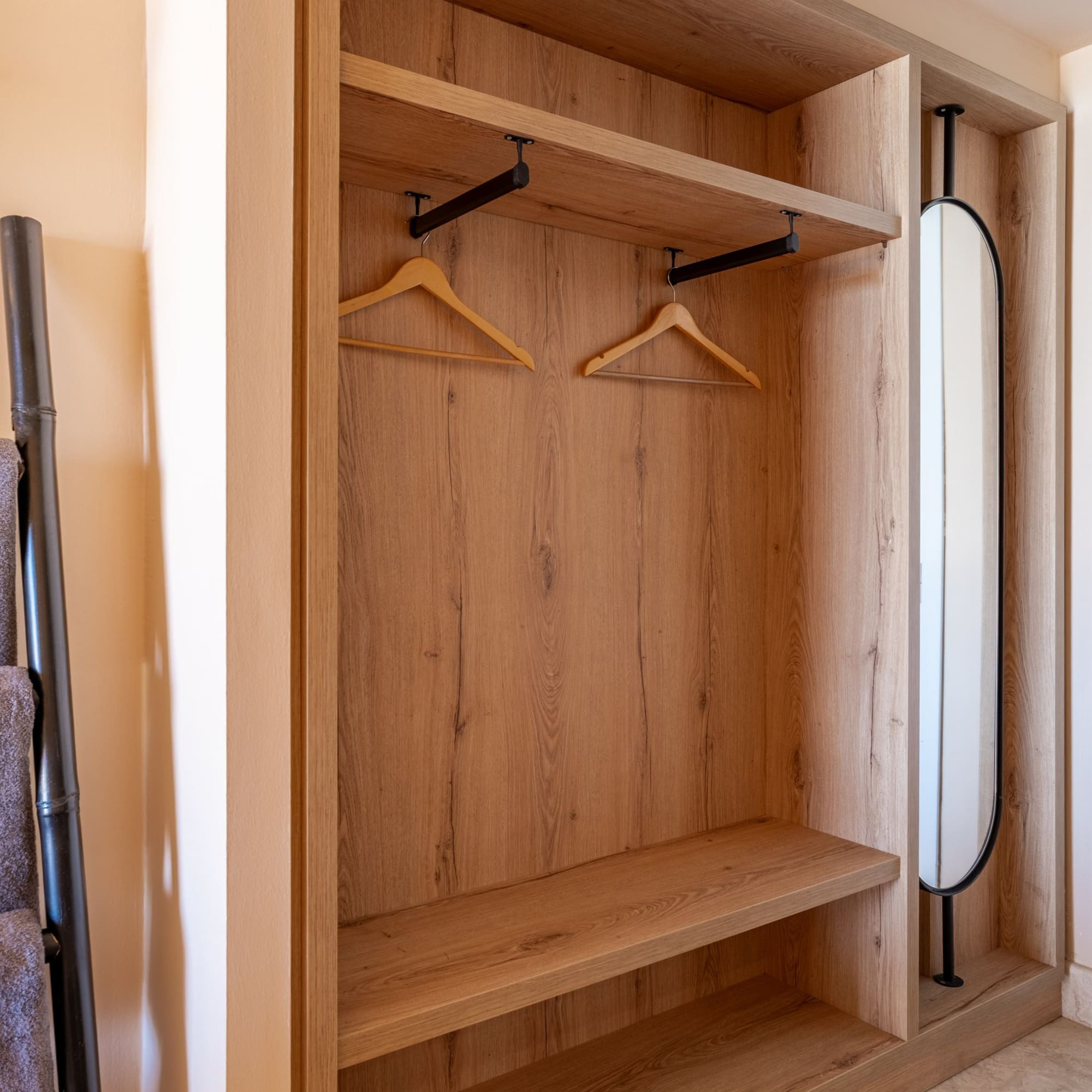 Modern light wood open wardrobe with hangers, shelves, and integrated mirror.