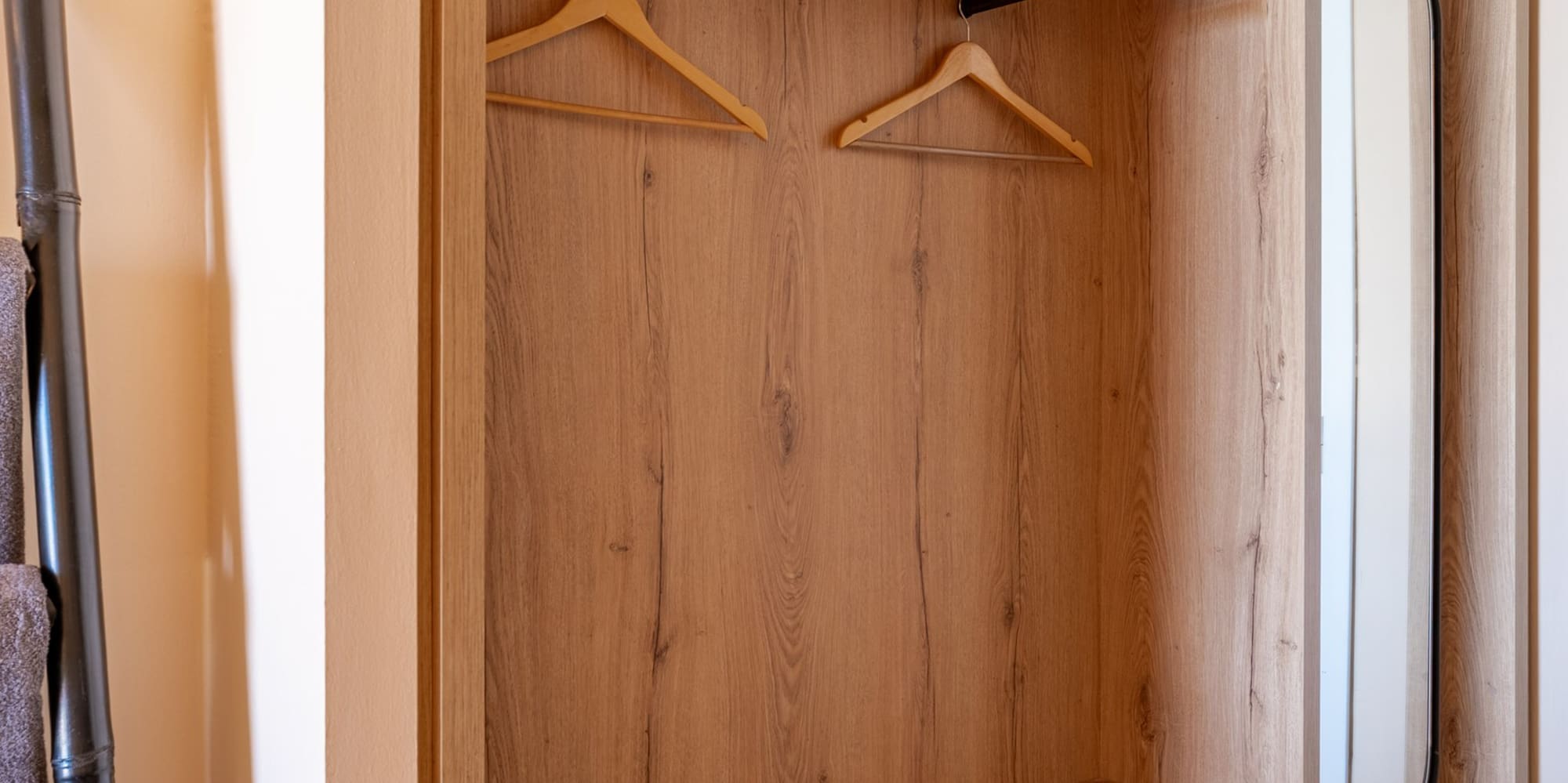 Modern light wood open wardrobe with hangers, shelves, and integrated mirror.