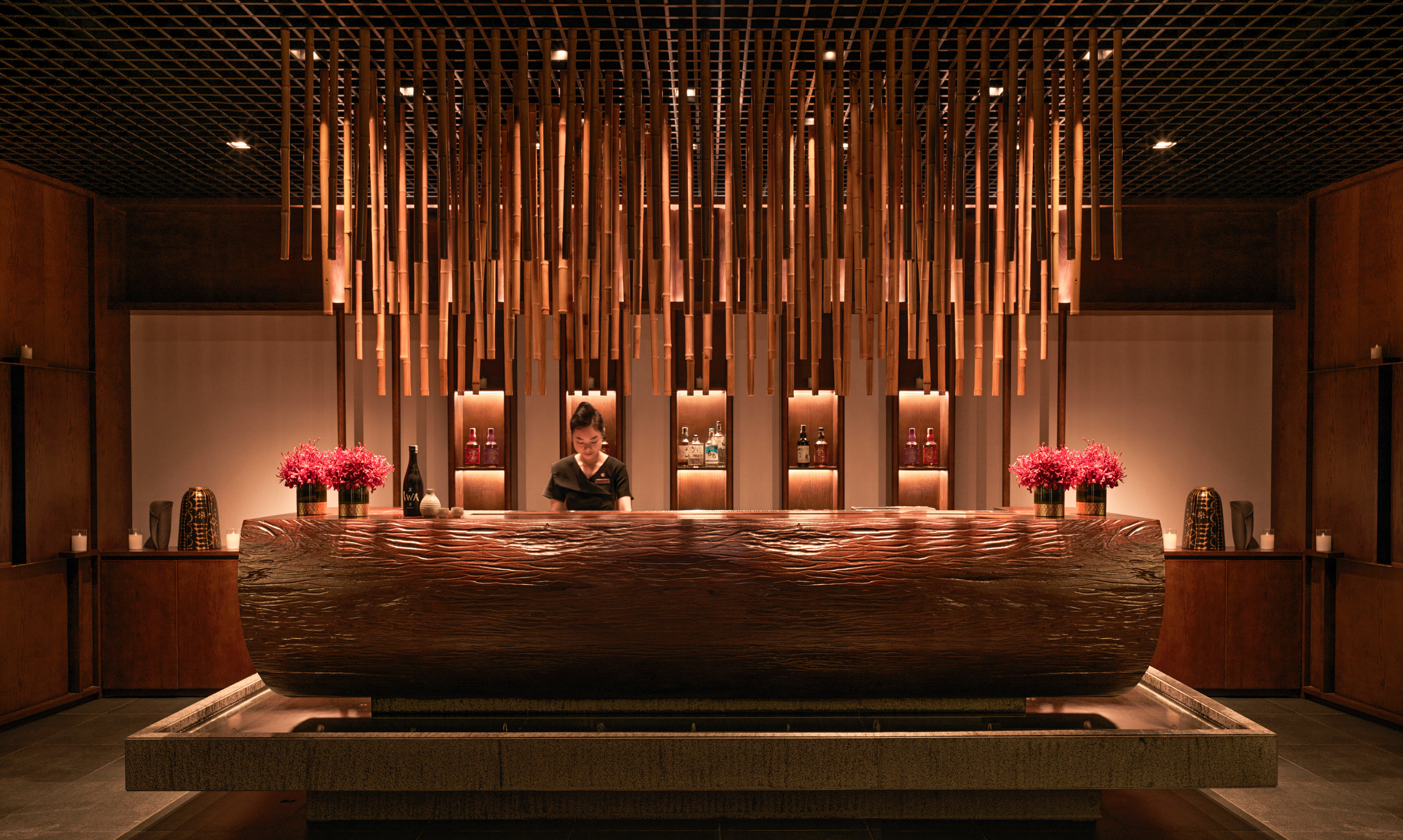 Luxury spa reception with carved wood desk, bamboo decor, and attendant.