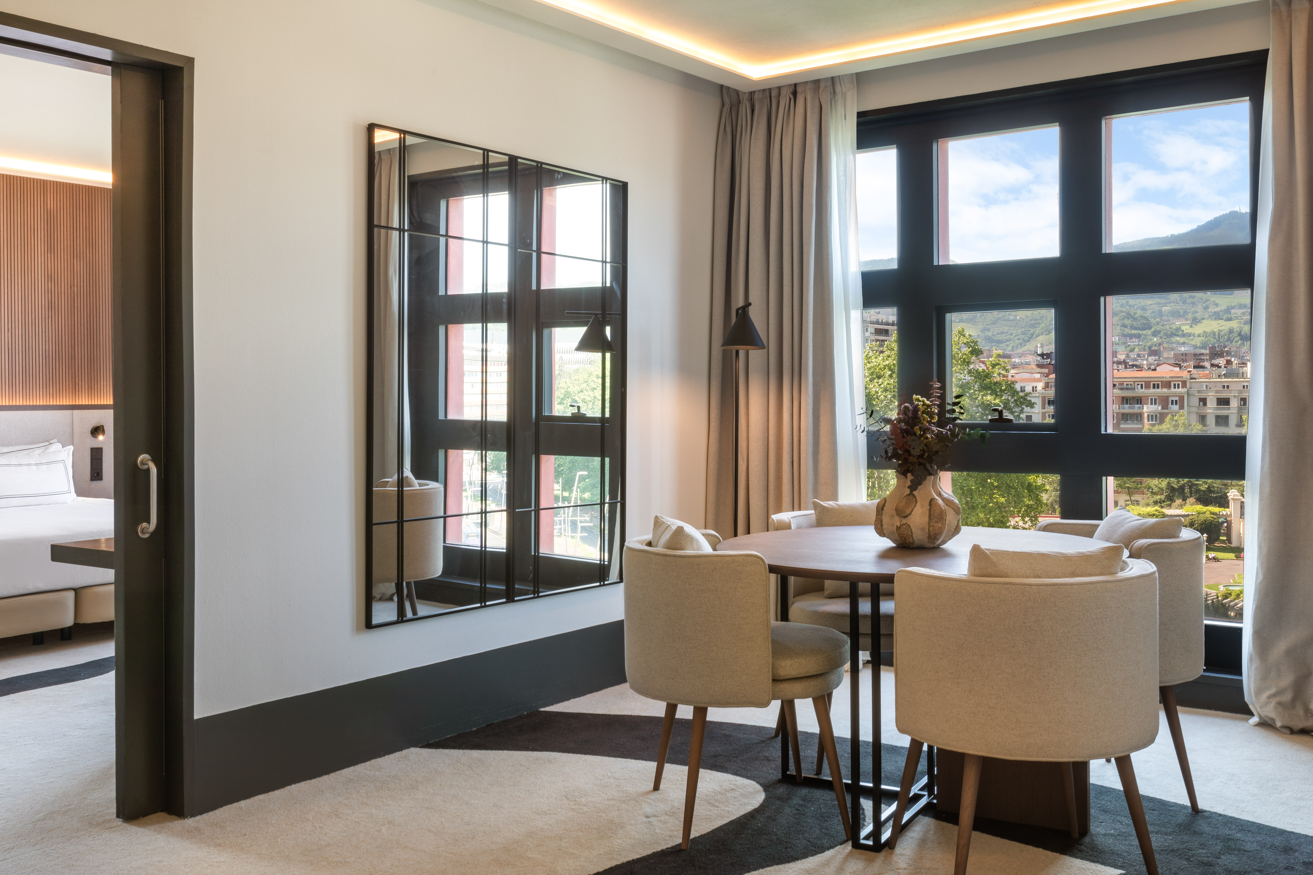 Modern hotel suite dining area with mountain view, round table, and bedroom entrance.