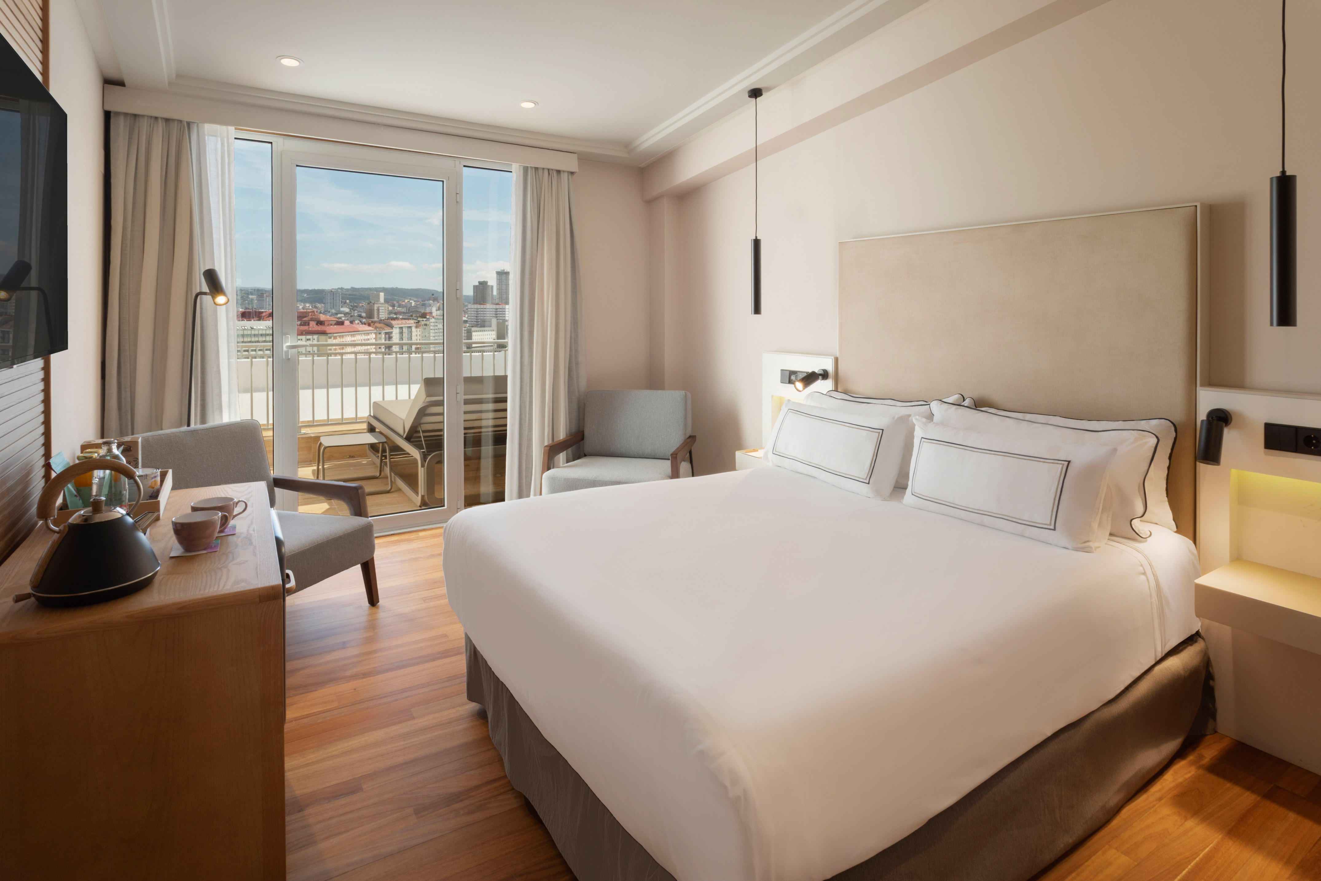 Spacious modern hotel bedroom with king bed, balcony city view, and wood floor.