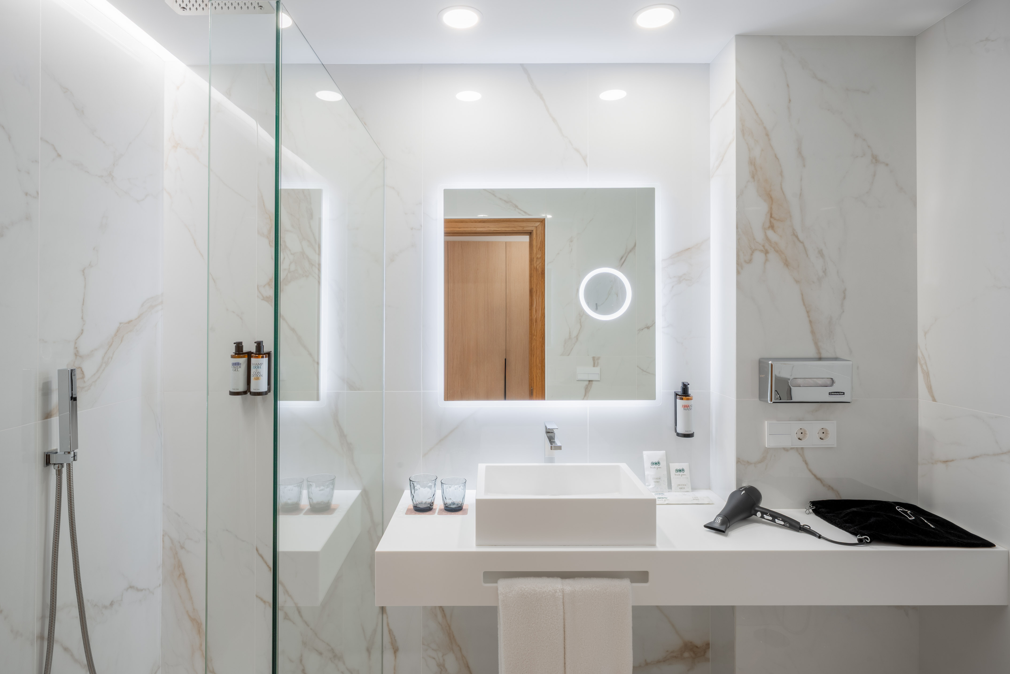 Luxury white marble bathroom with lighted mirror, floating vanity, and shower.