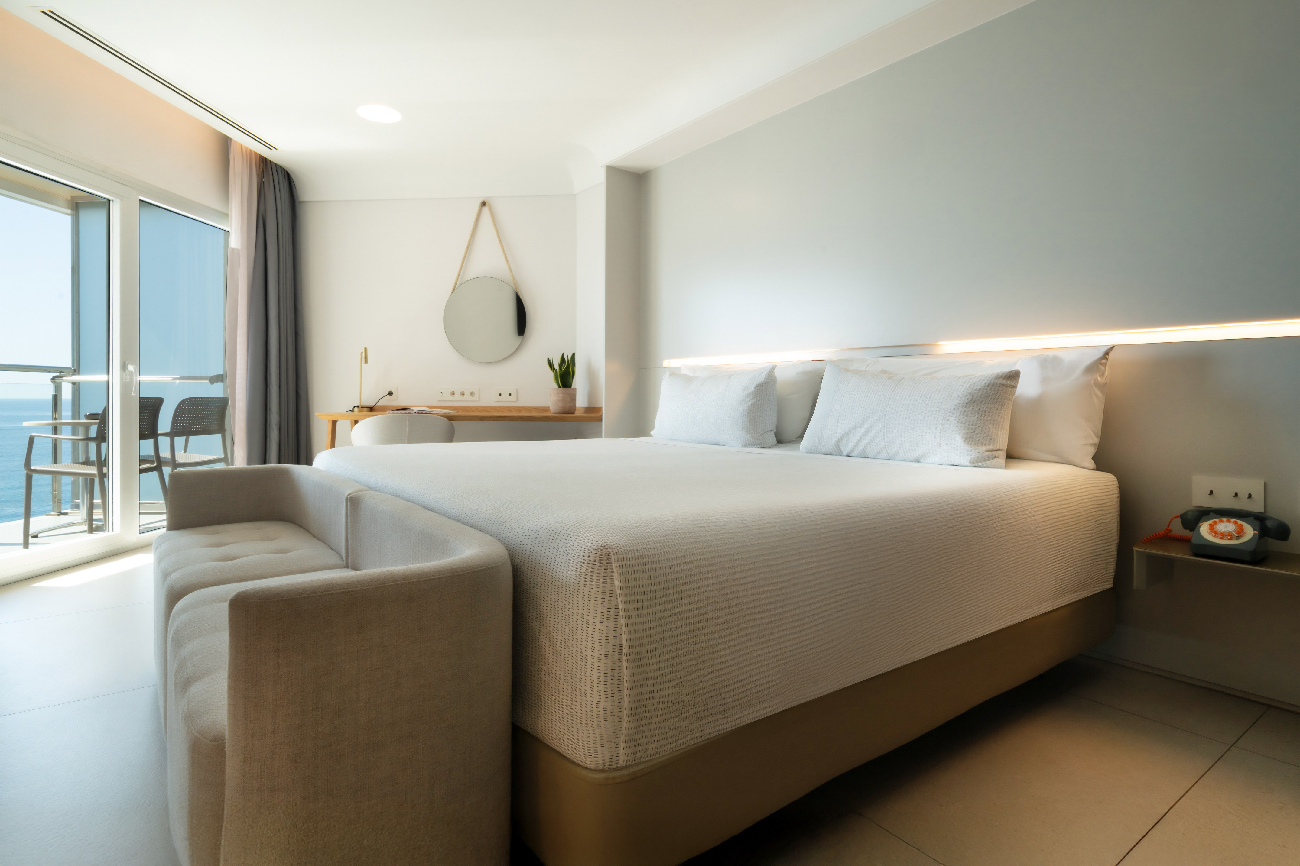 Modern hotel bedroom with large bed, ocean view balcony, and sofa.