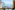 Coastal balcony view with palm trees, boats, and clear blue ocean.