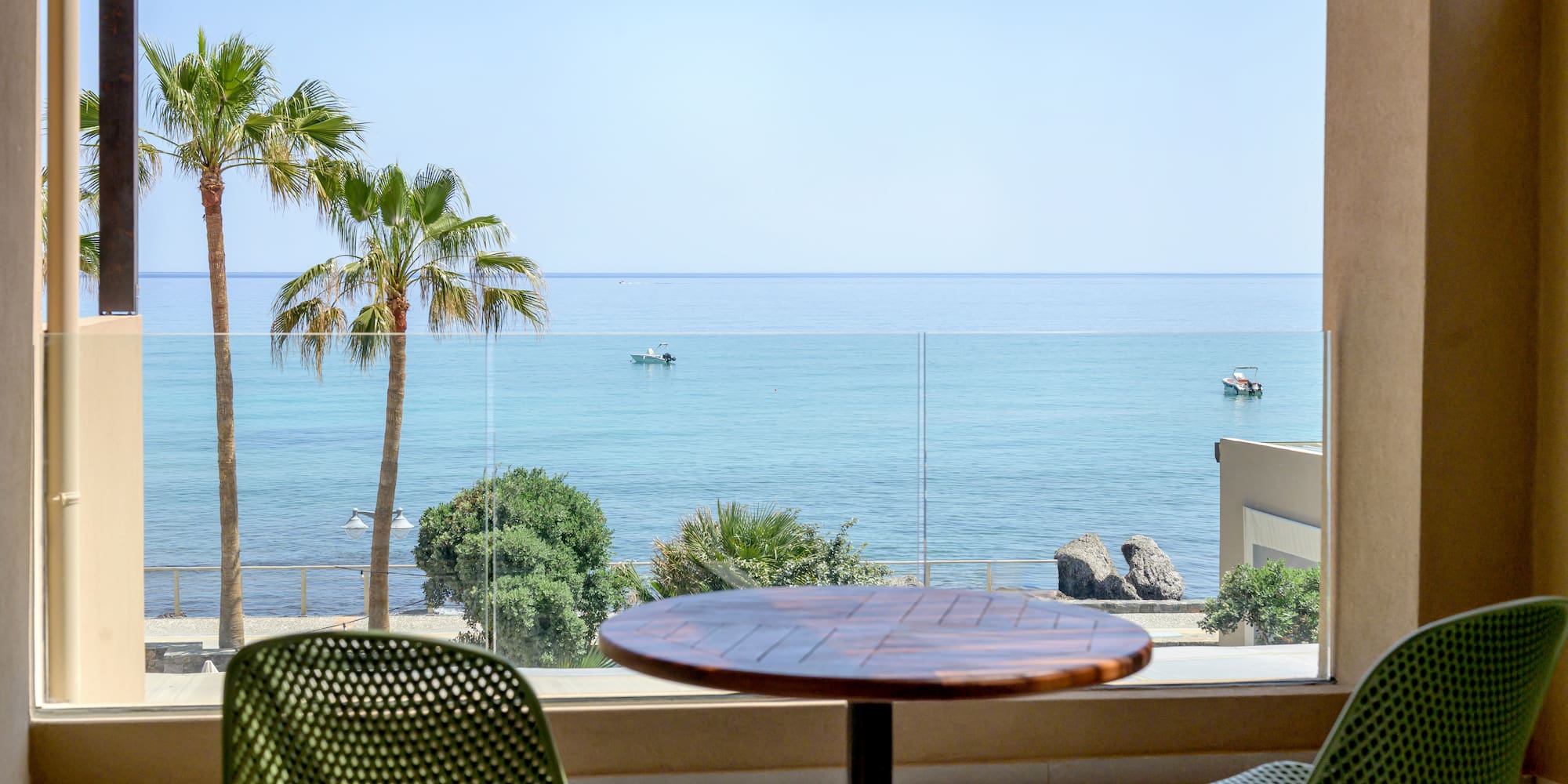 Coastal balcony view with palm trees, boats, and clear blue ocean.