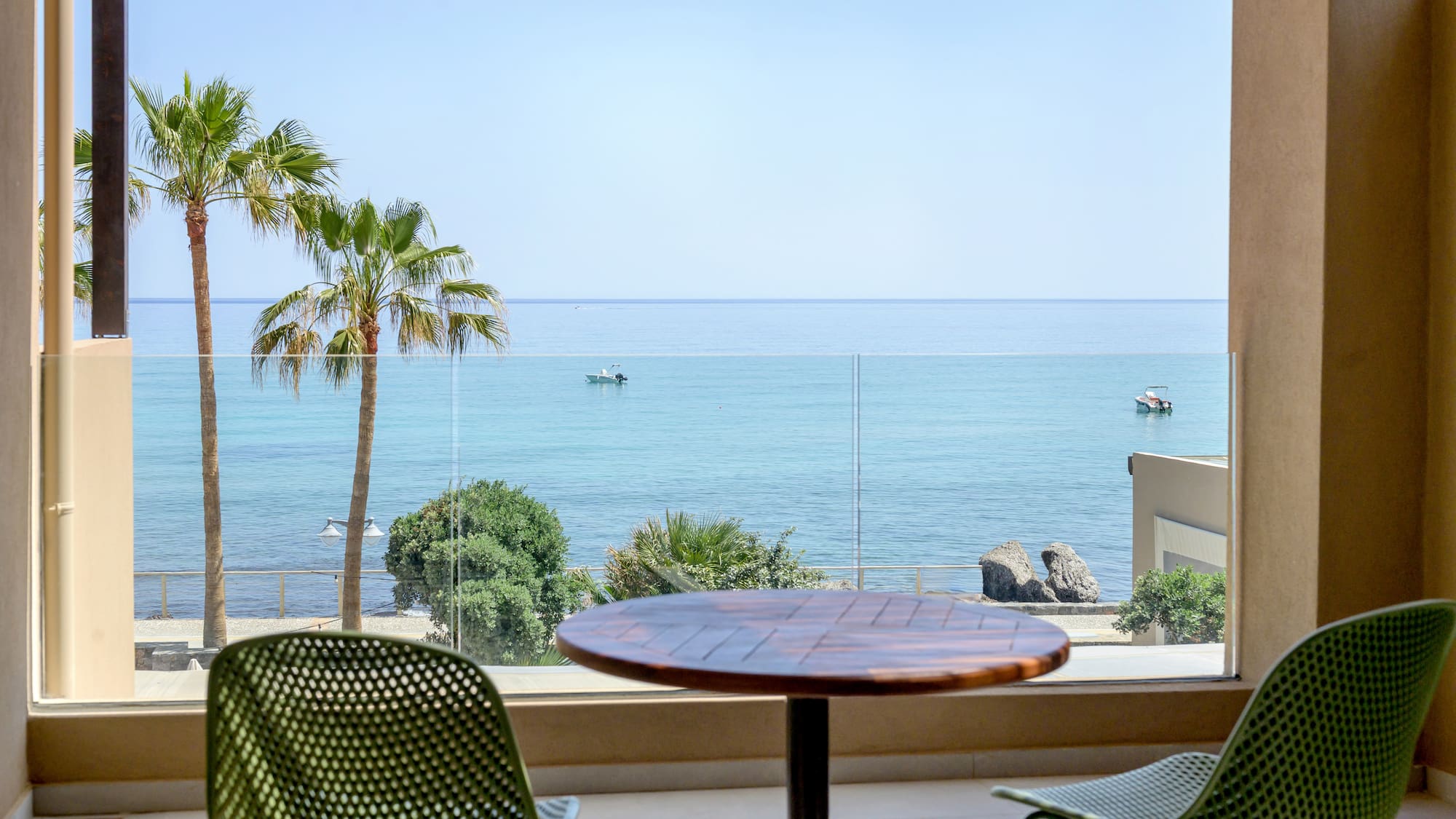 Coastal balcony view with palm trees, boats, and clear blue ocean.