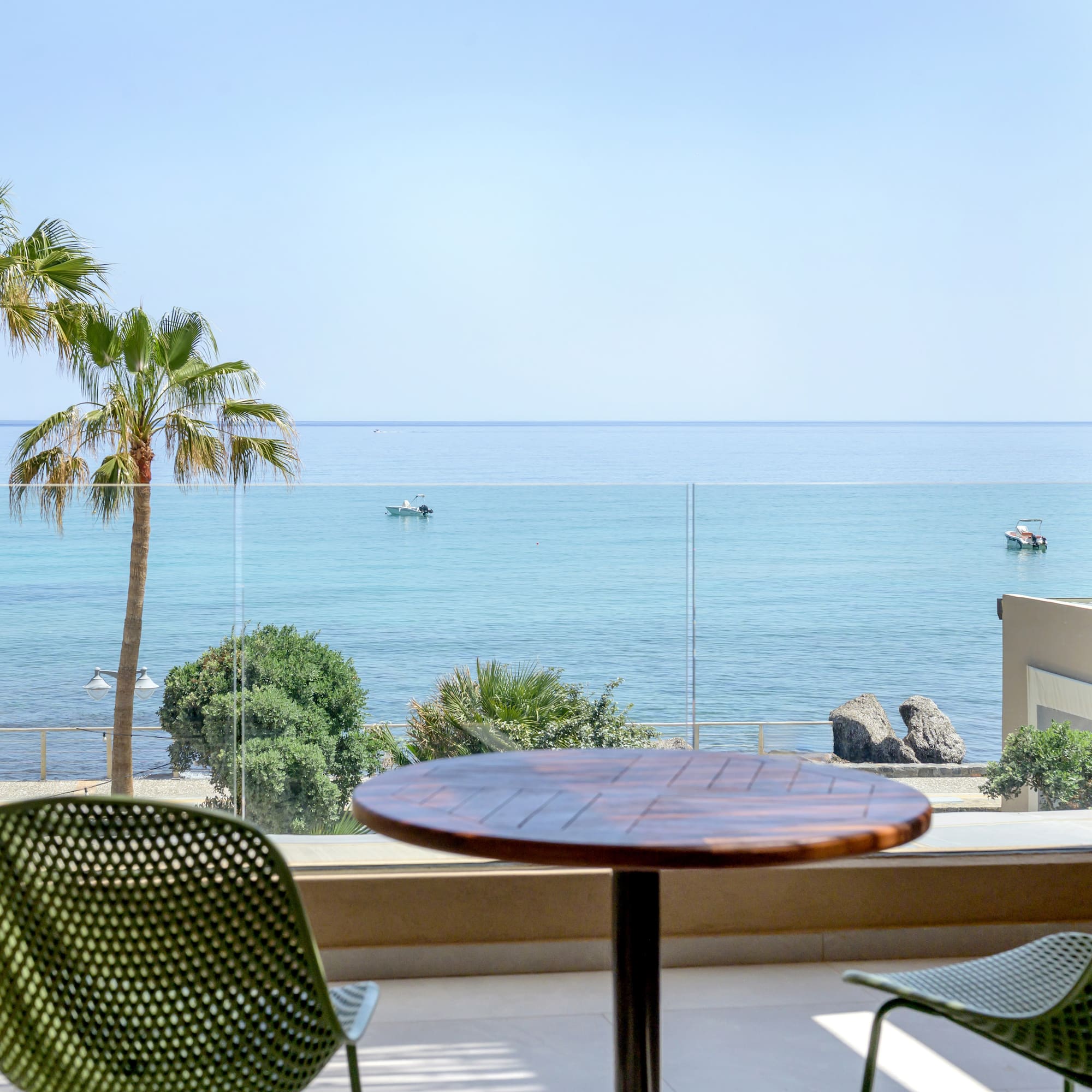 Coastal balcony view with palm trees, boats, and clear blue ocean.