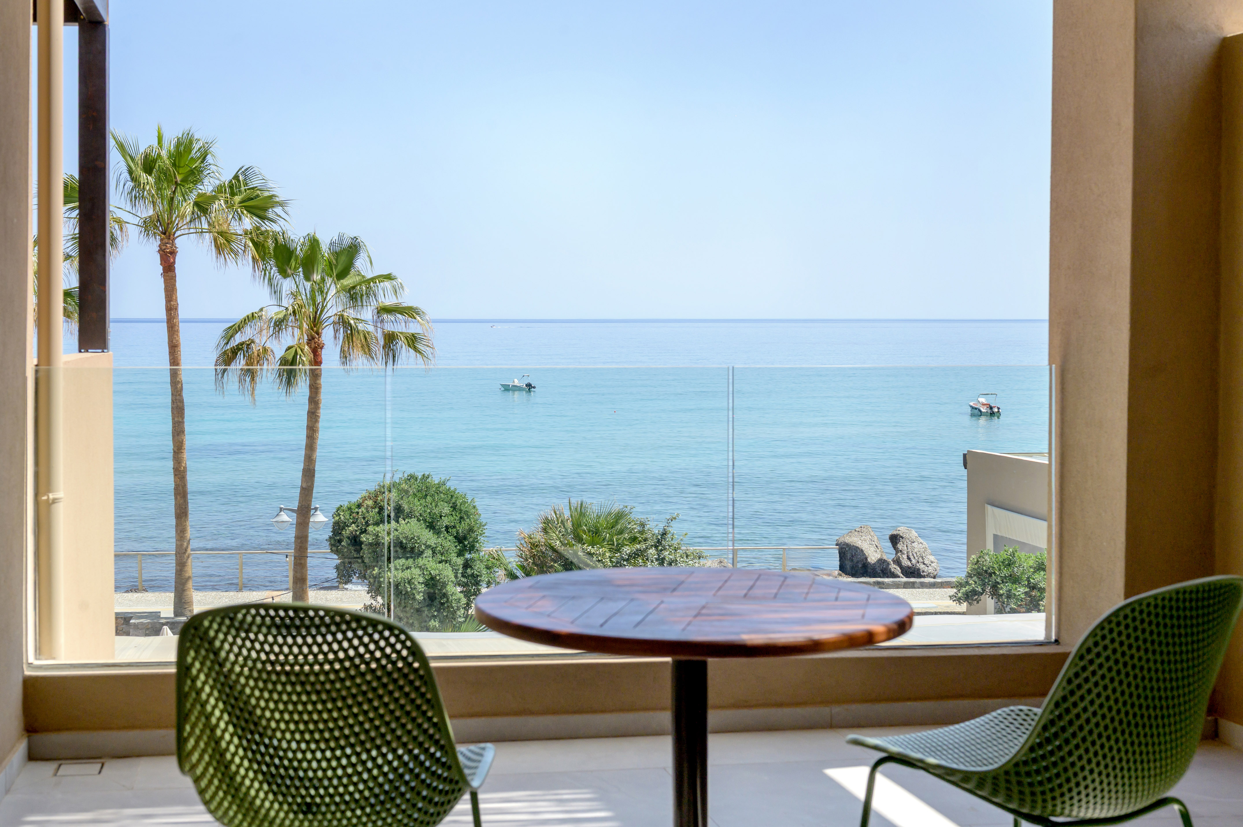Coastal balcony view with palm trees, boats, and clear blue ocean.