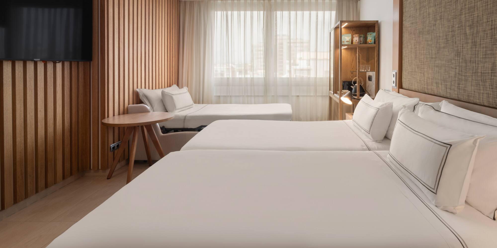 Modern hotel room with twin beds, a sofa bed, wood paneling, and TV.