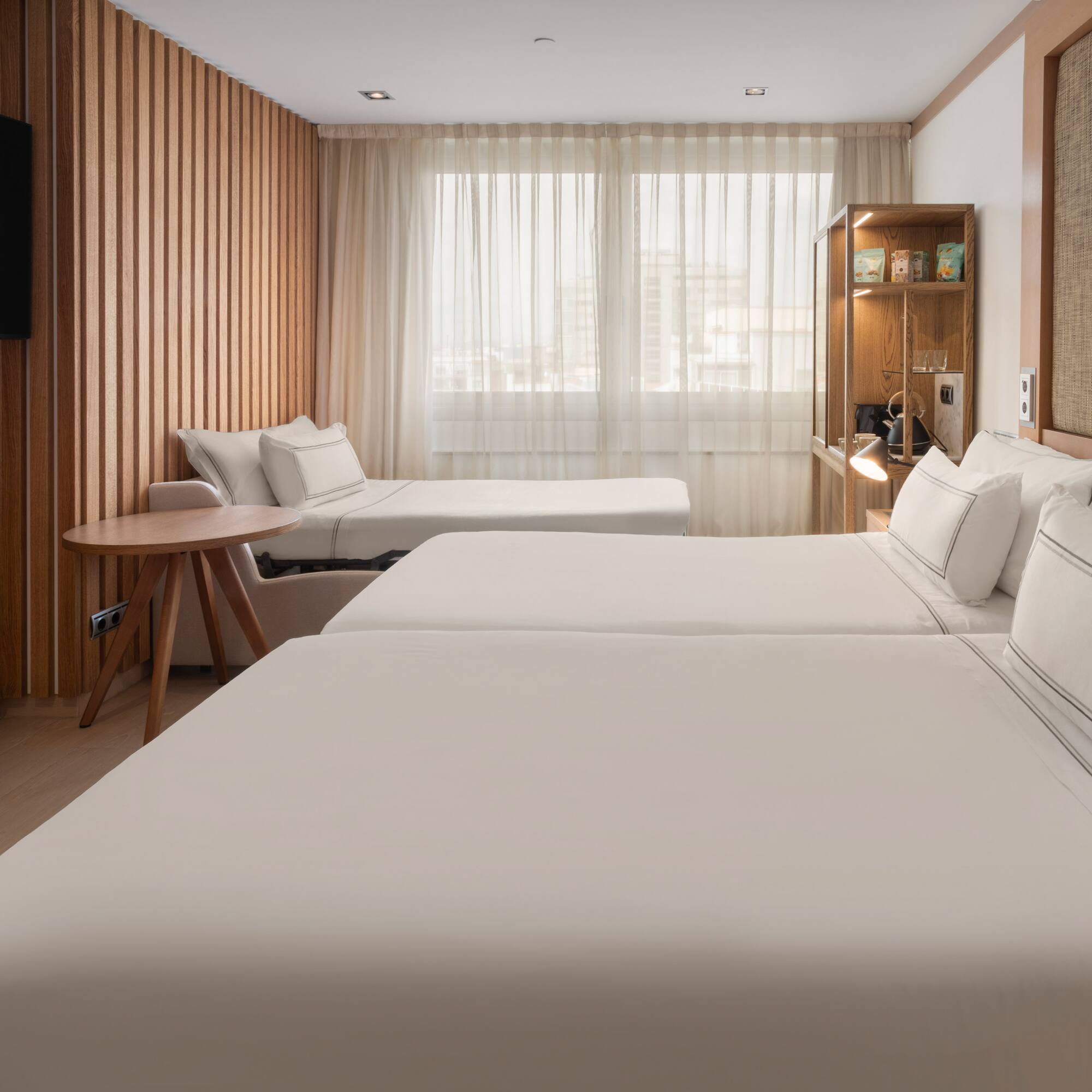 Modern hotel room with twin beds, a sofa bed, wood paneling, and TV.