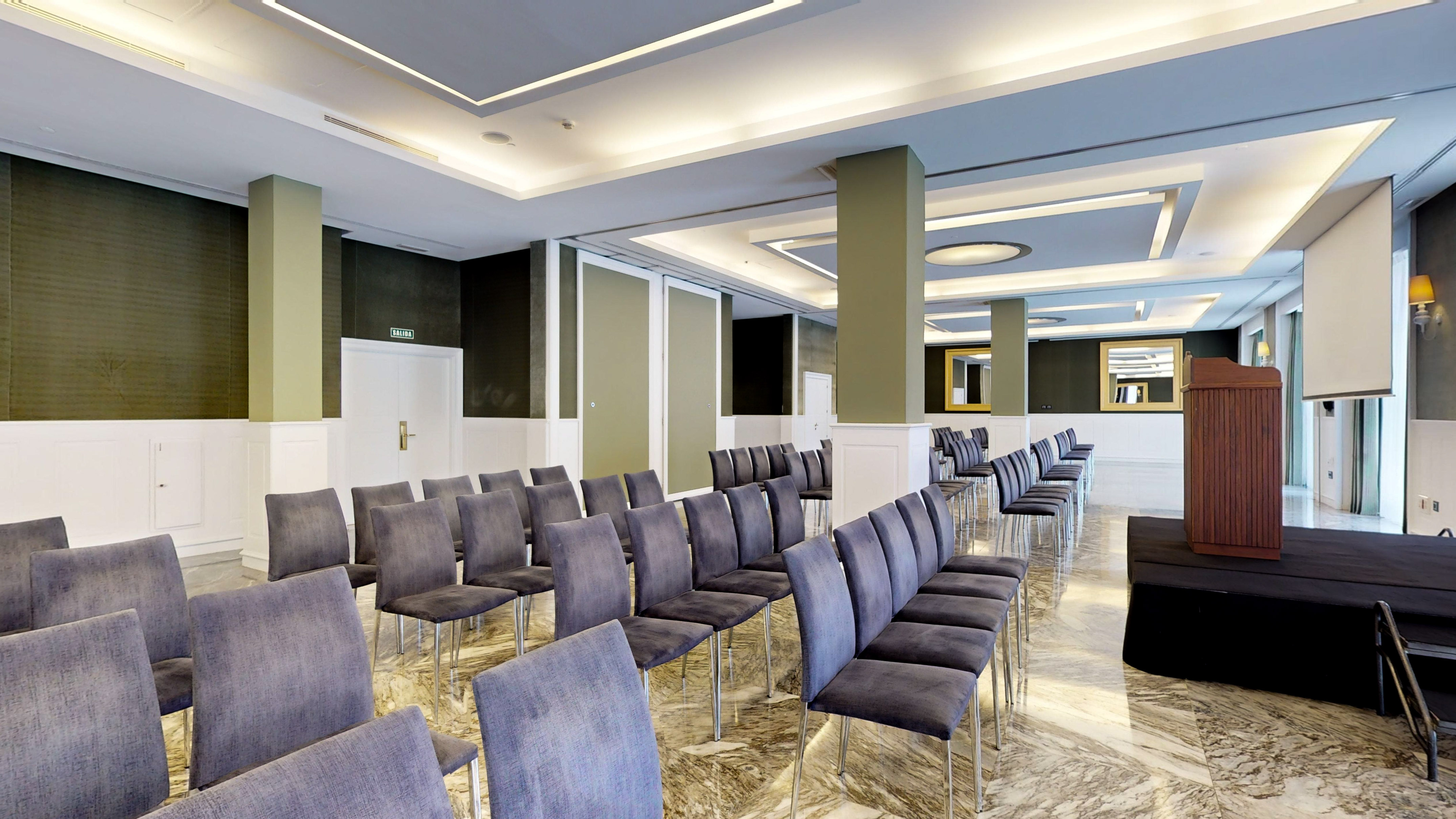 Modern meeting room with grey chairs, lectern, and projection screen.