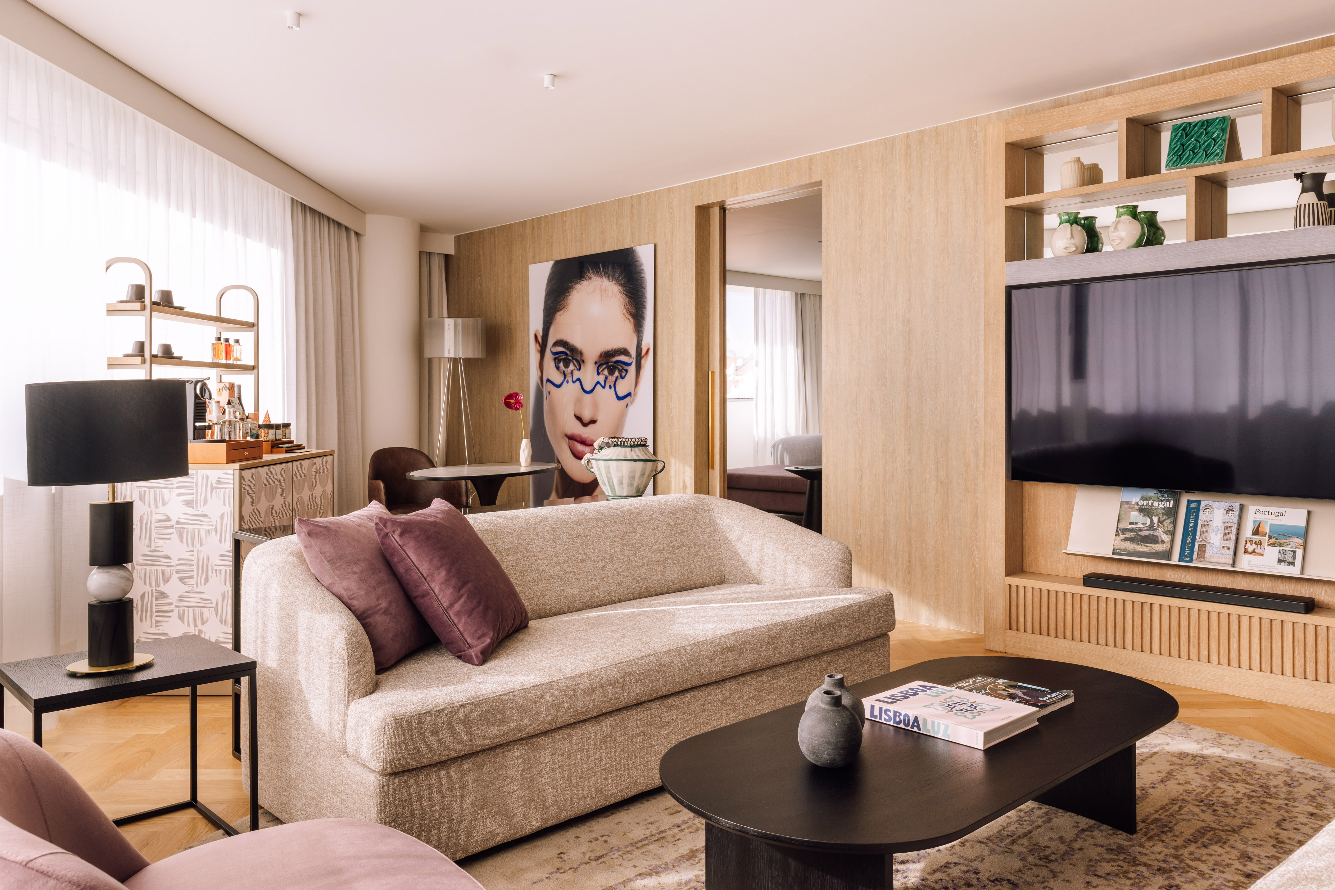 Modern hotel living room: beige sofa, wooden media unit, and abstract wall art.
