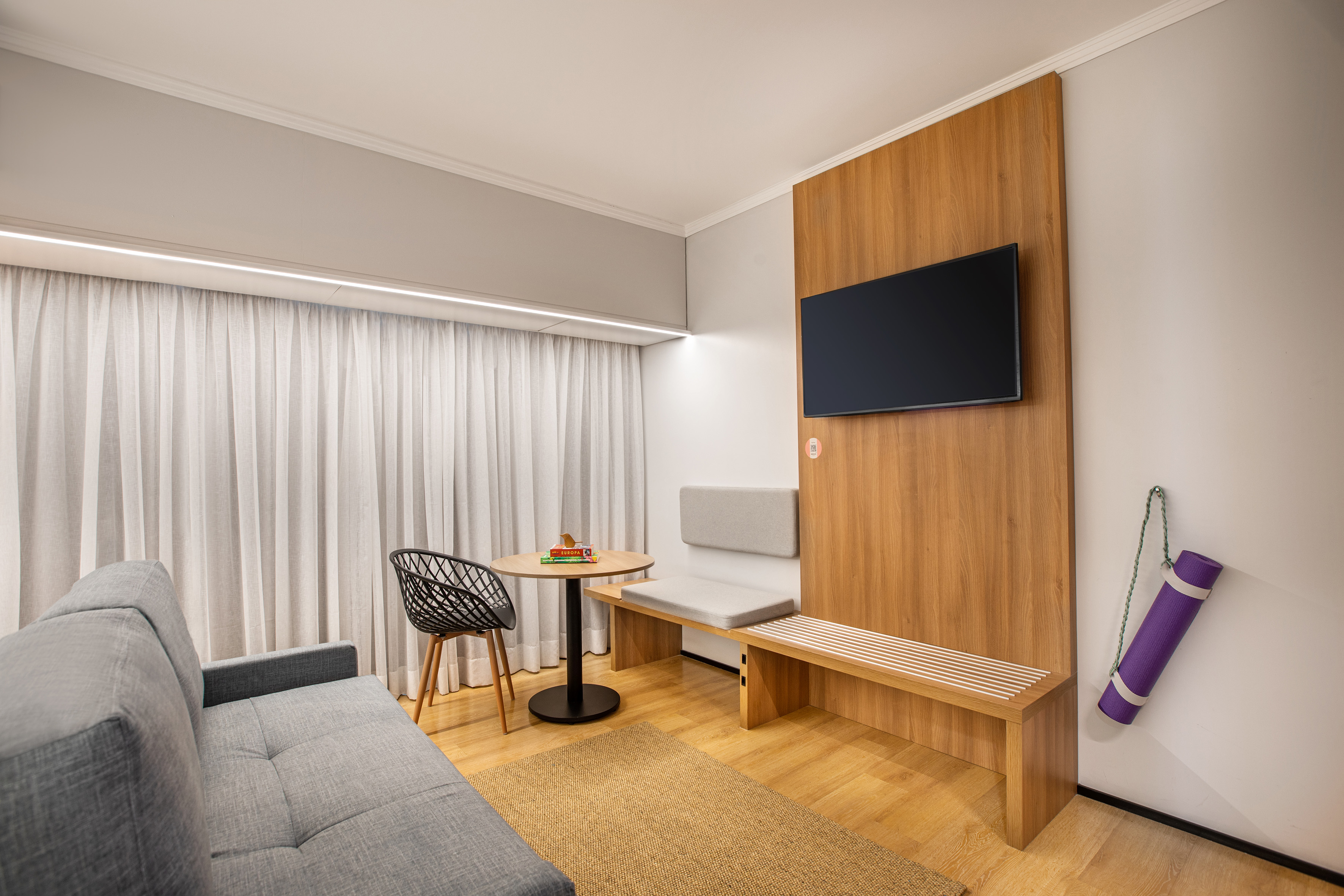 Stylish living space with TV, grey sofa, wooden bench, and yoga mat.