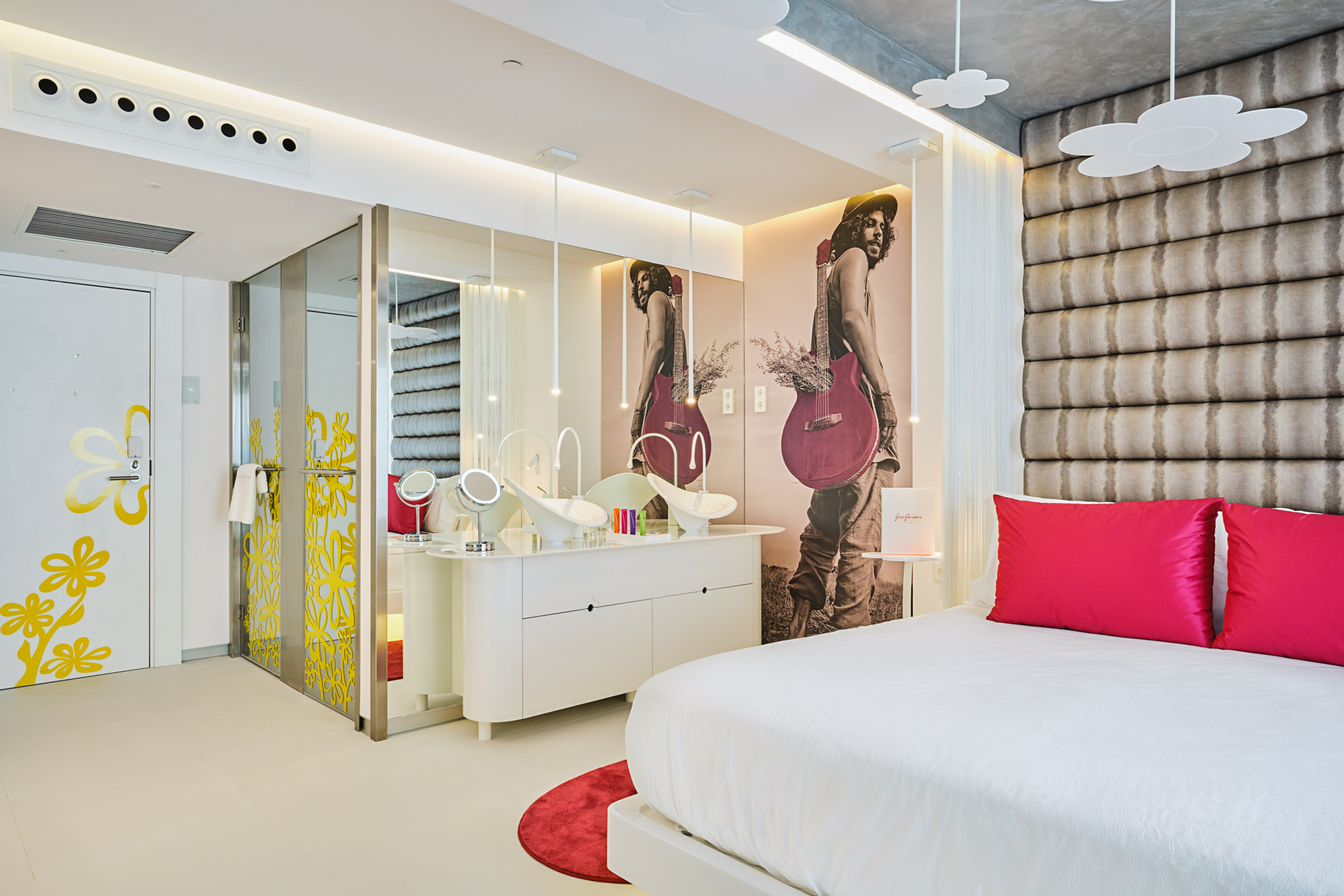Stylish hotel room with white bed, red pillows, guitar mural, and double vanity.