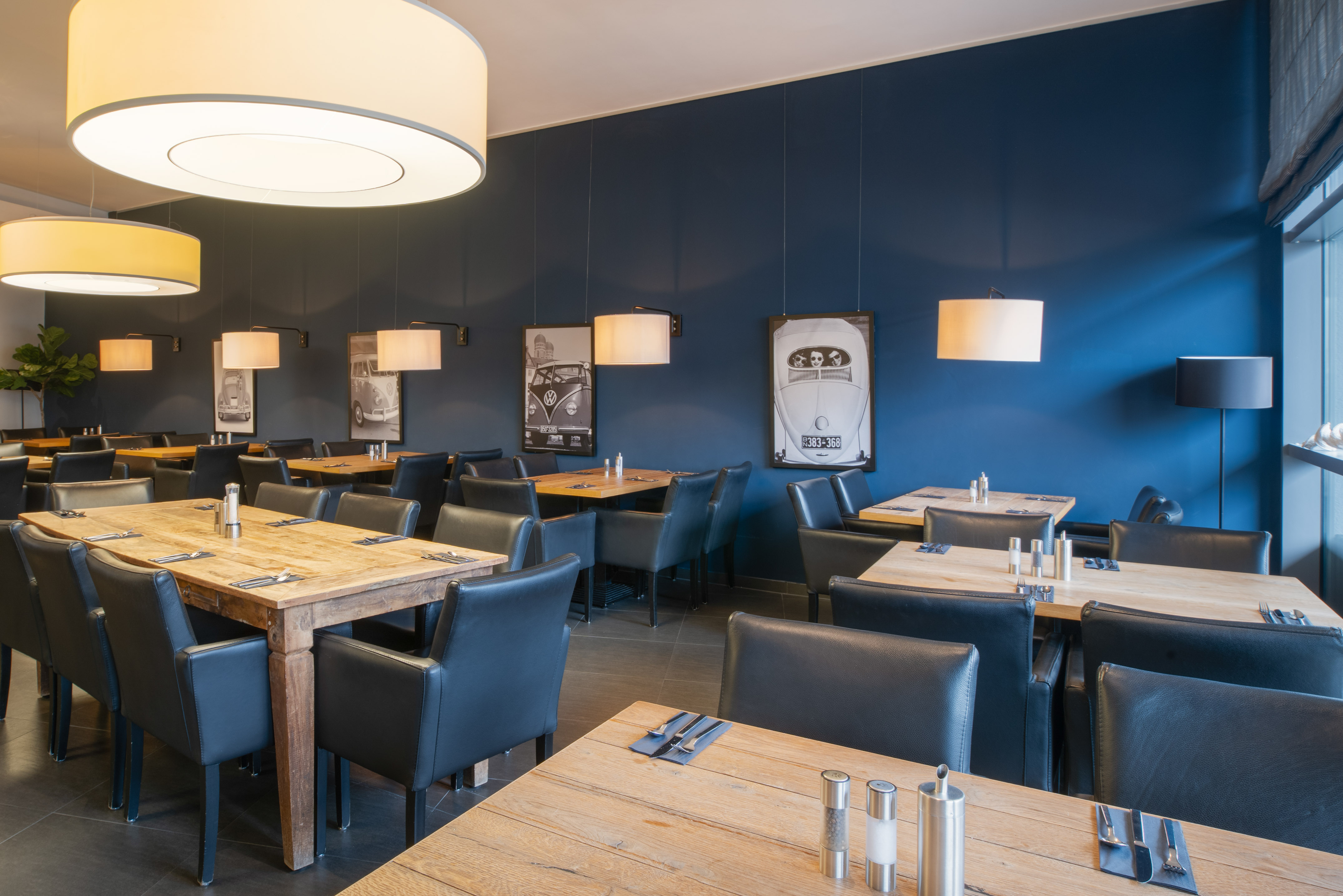 Restaurant with wooden tables, black chairs, blue walls, car art.