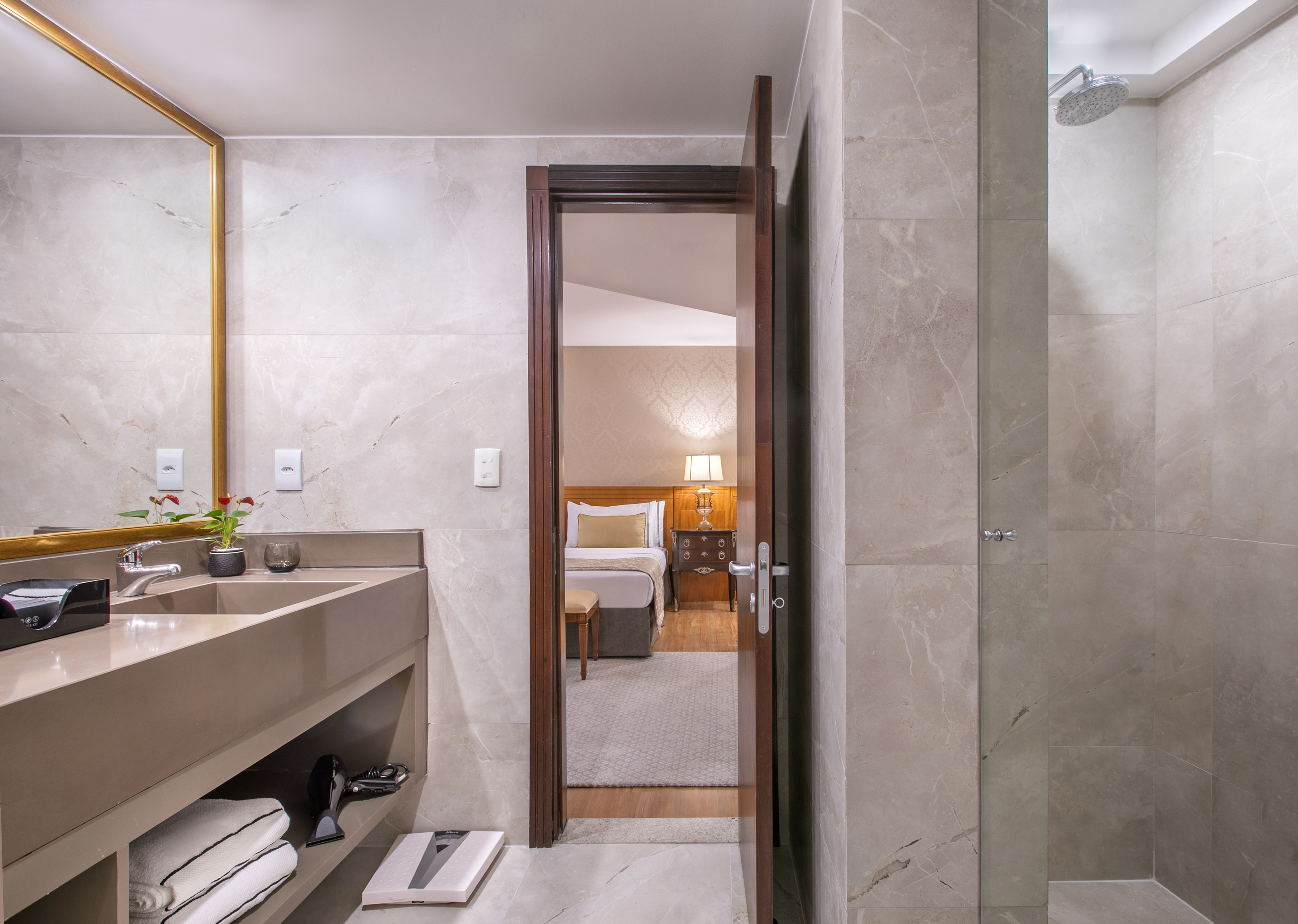 Modern hotel bathroom with vanity, shower, and open doorway to a cozy bedroom.