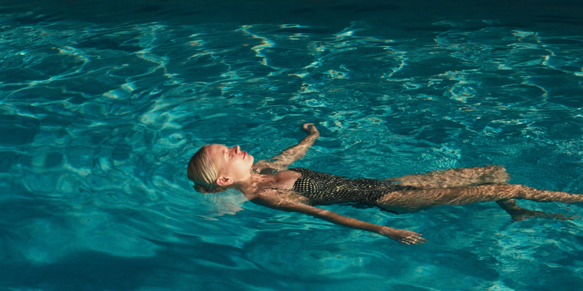 Relaxed blonde woman floating on her back in a blue swimming pool.