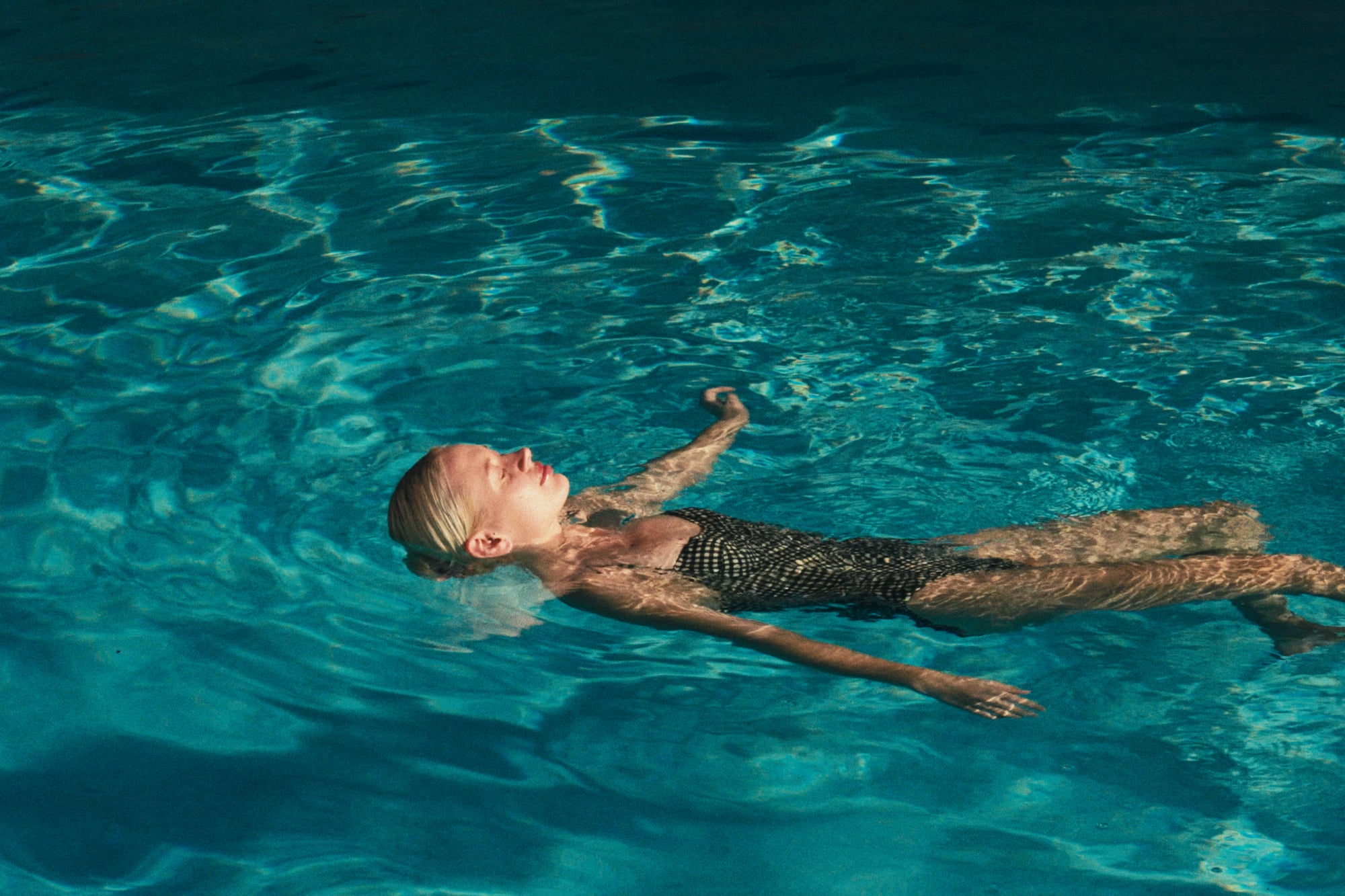 Blonde woman floating on her back in a clear blue swimming pool.