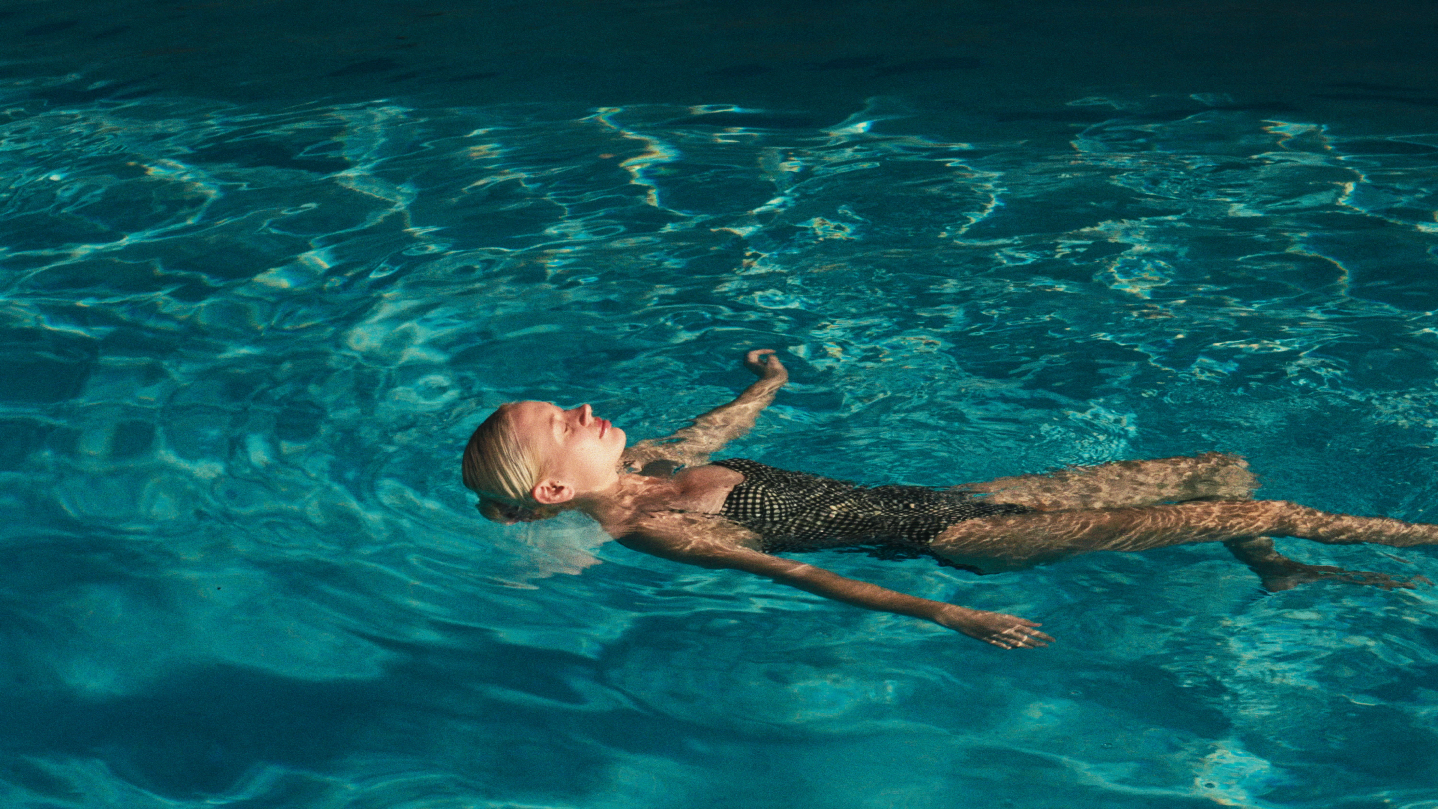 Relaxed blonde woman floating on her back in a blue swimming pool.