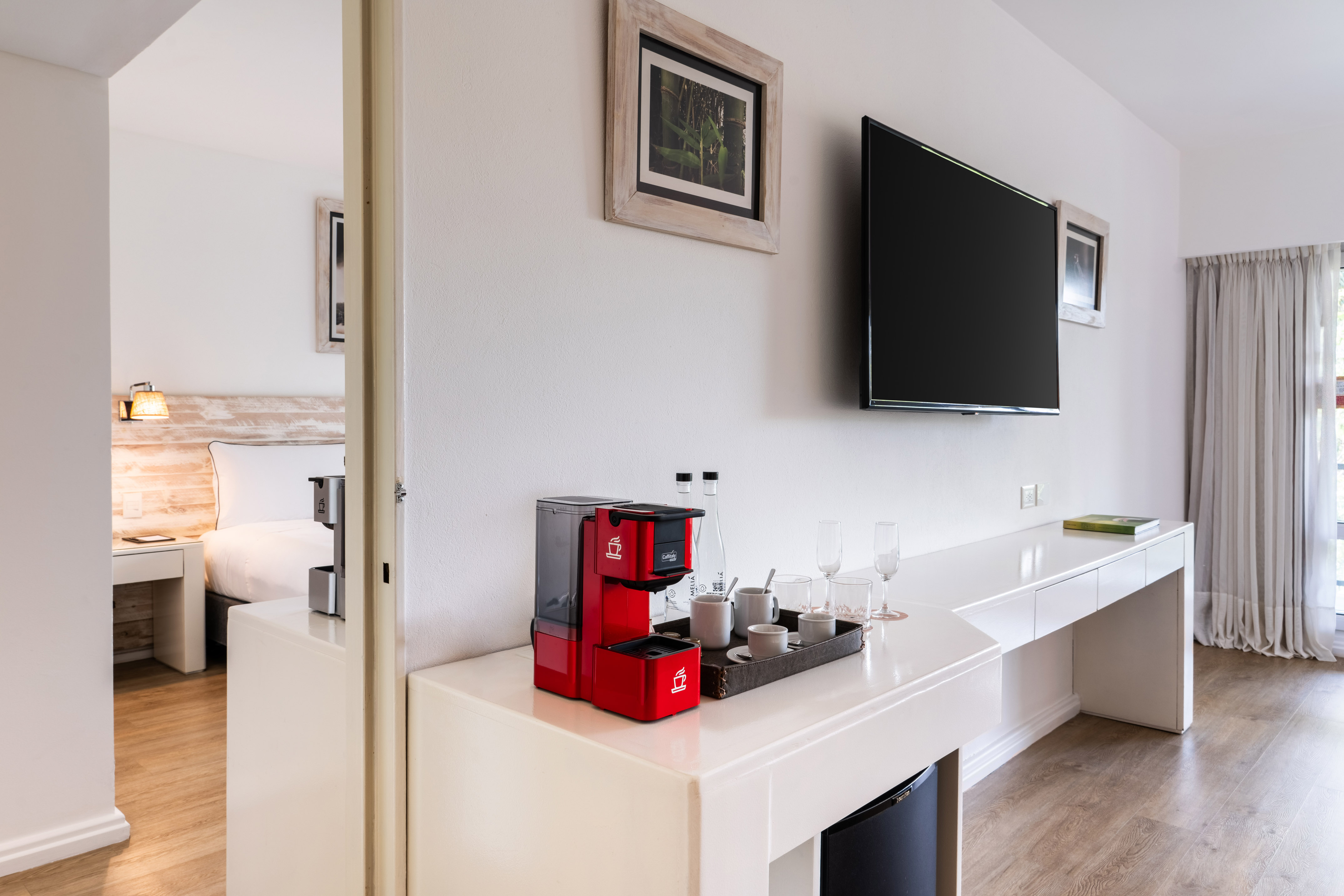 Hotel suite with red coffee maker, flat-screen TV, and a glimpse of the bedroom.
