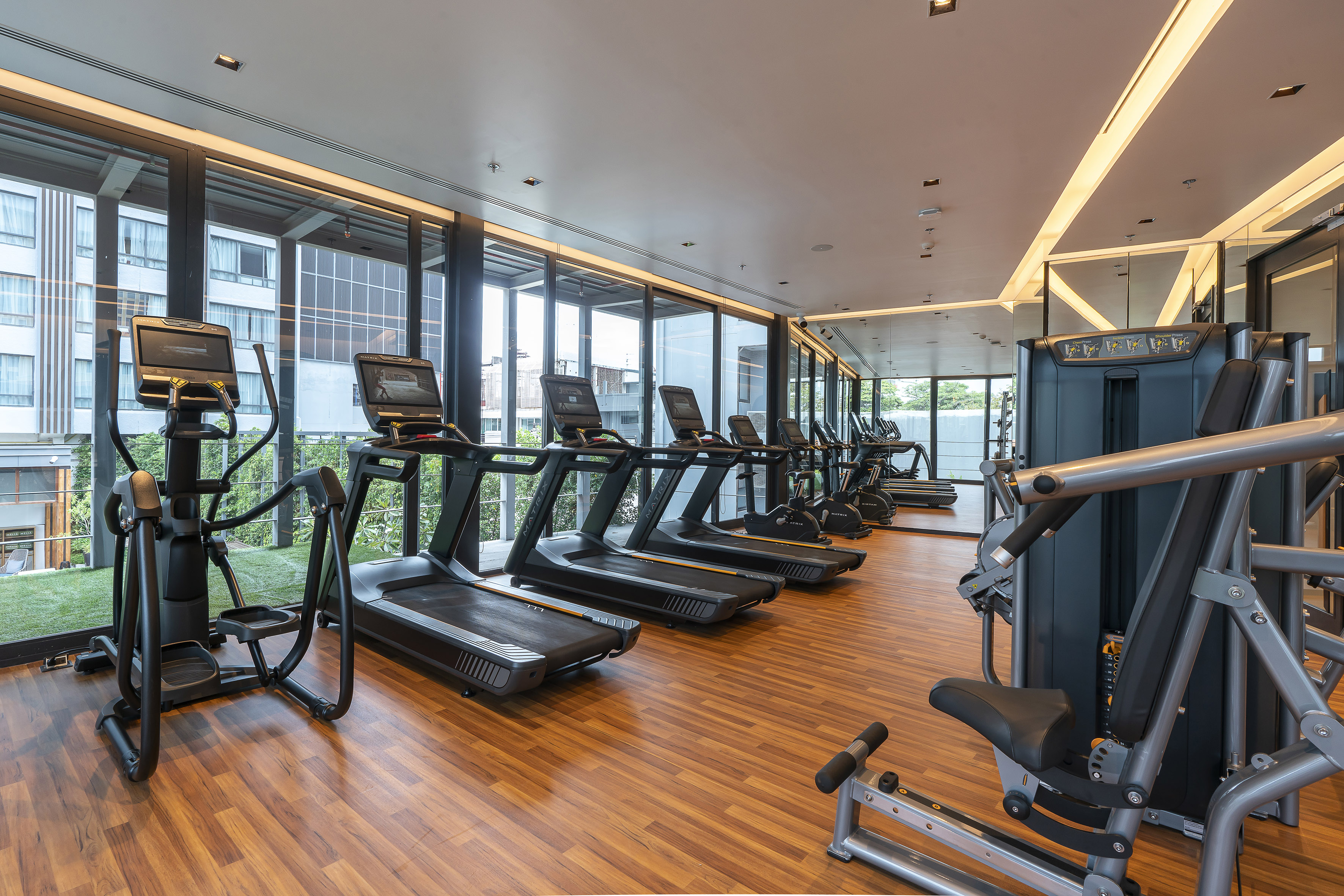 Modern gym with rows of treadmills, an elliptical, weight machine, and large windows.