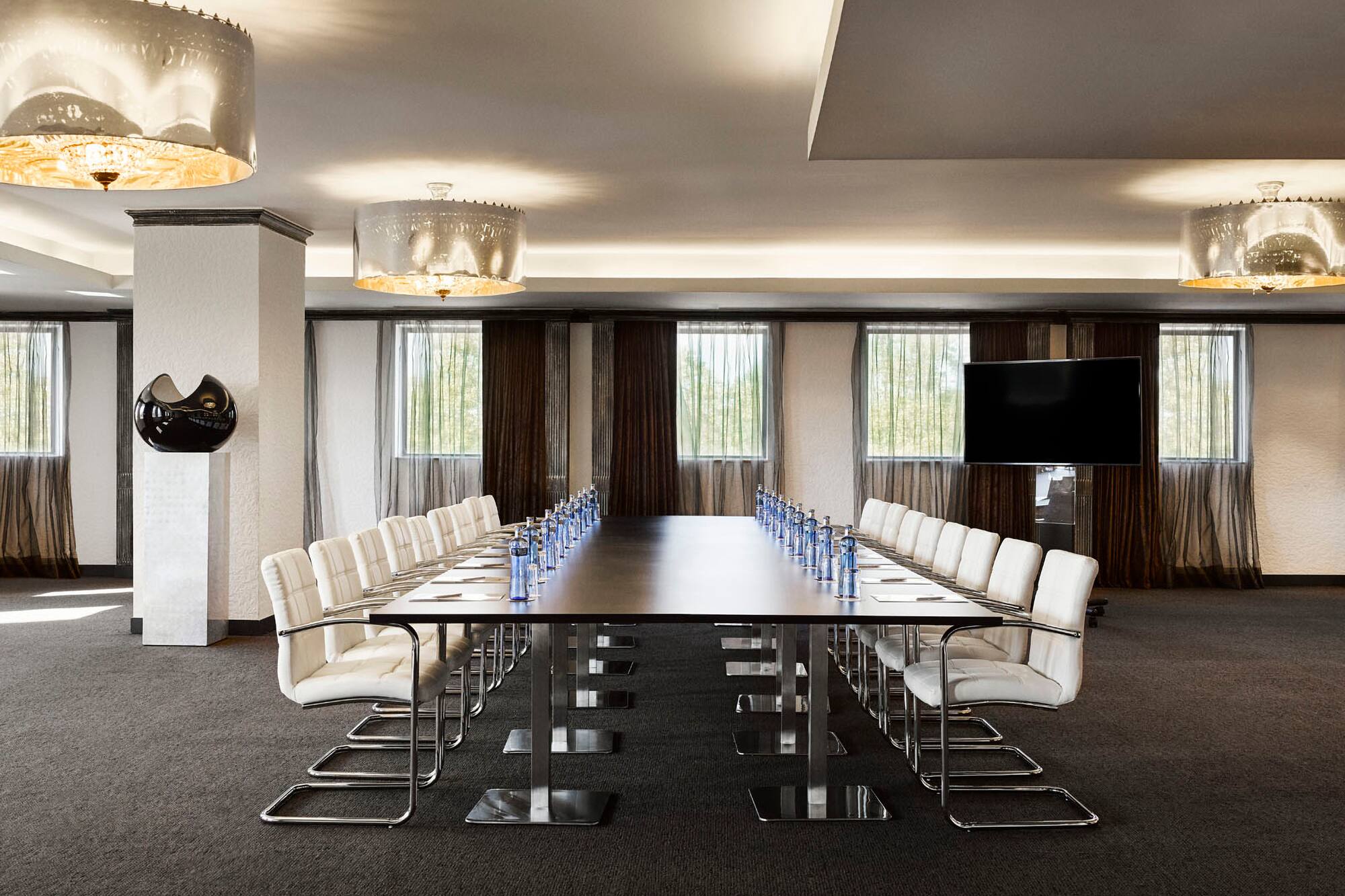 Modern conference room with long table, executive chairs, and large TV screen.